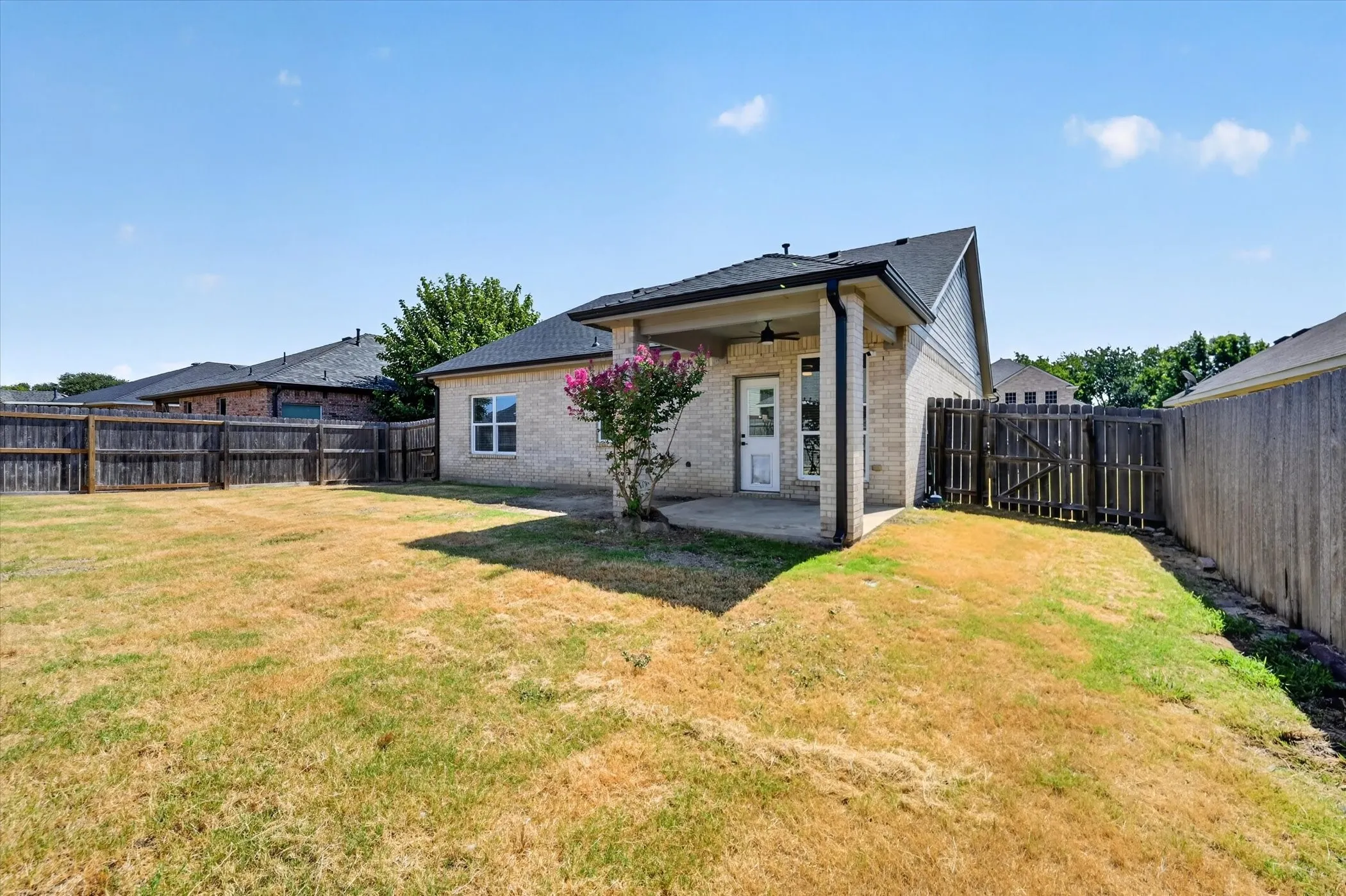 Expansive backyard featuring a covered patio, brick exterior, and wood fencing