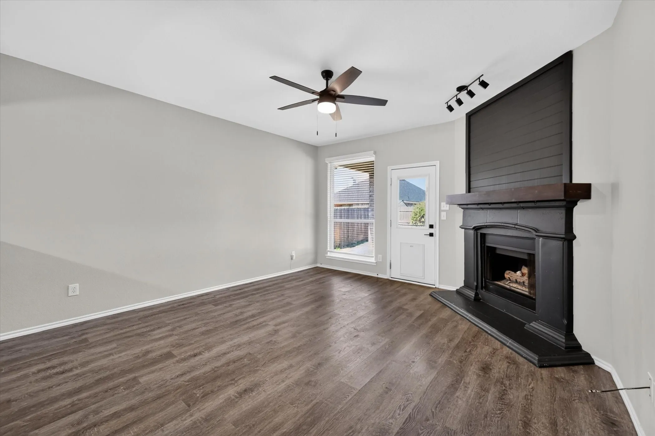 Wood-finish flooring throughout, a ceiling fan with integrated lighting, and a corner-set fireplace with a dark mantel