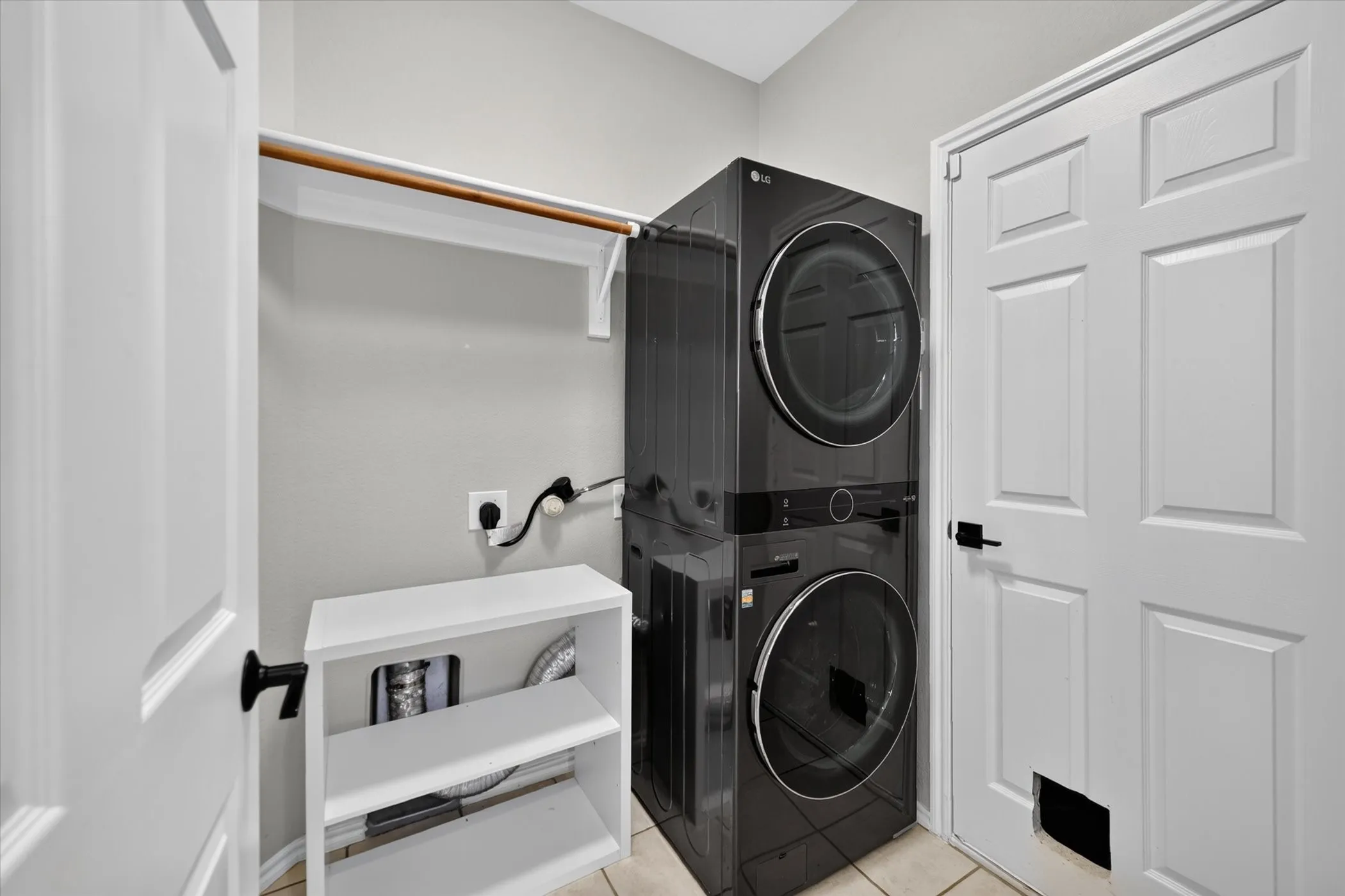 Laundry area featuring a stackable washer and dryer, white shelving unit, and tile flooring
