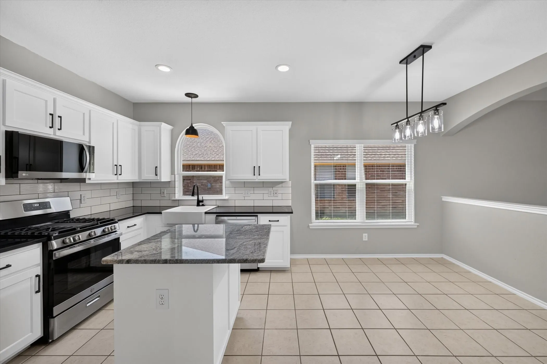 Kitchen featuring white cabinetry, subway tile backsplash, stainless steel appliances, a center island with a stone countertop, and tile flooring
