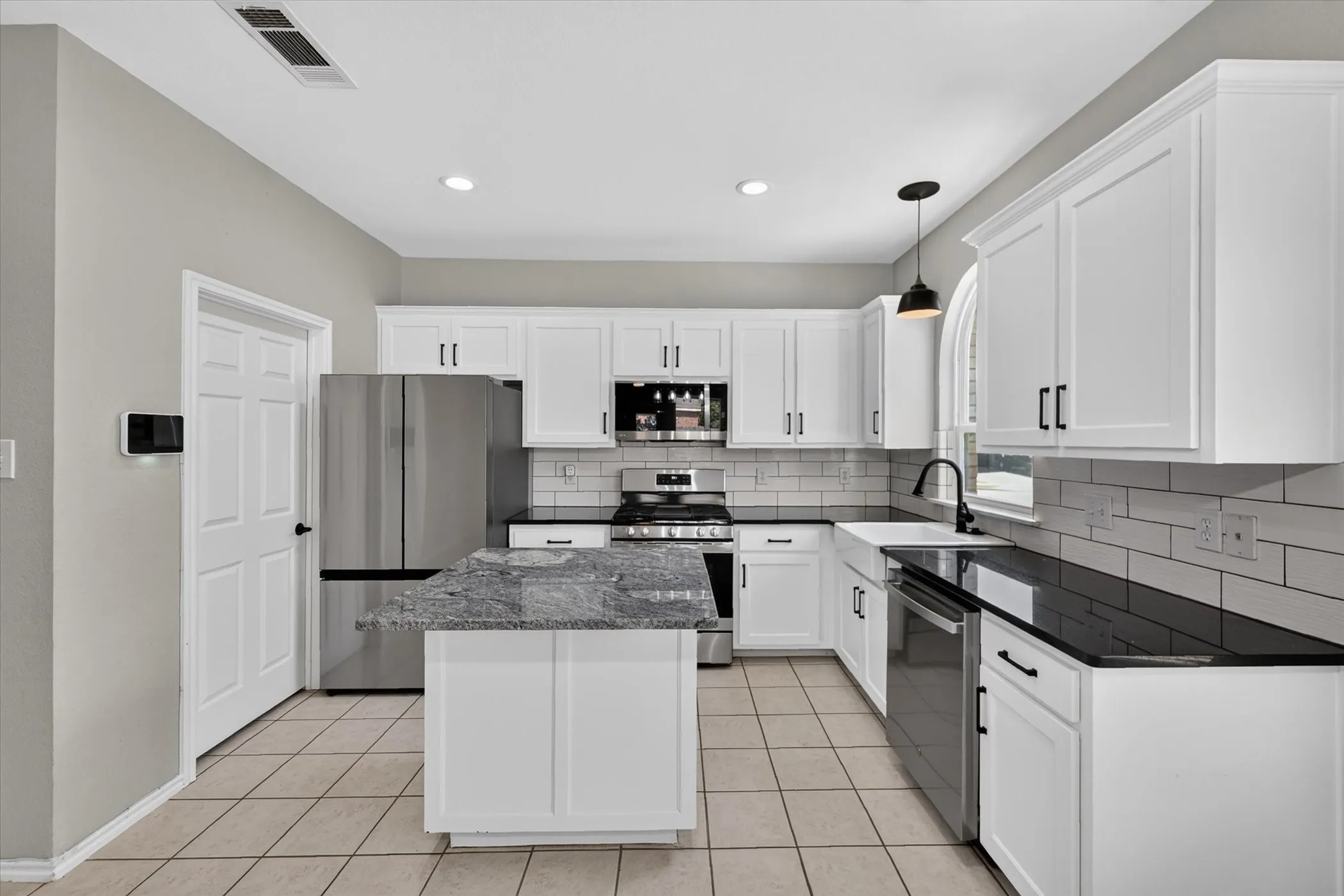 White cabinetry with black hardware, stainless steel appliances, tile flooring, subway tile backsplash, and a kitchen island with stone countertop