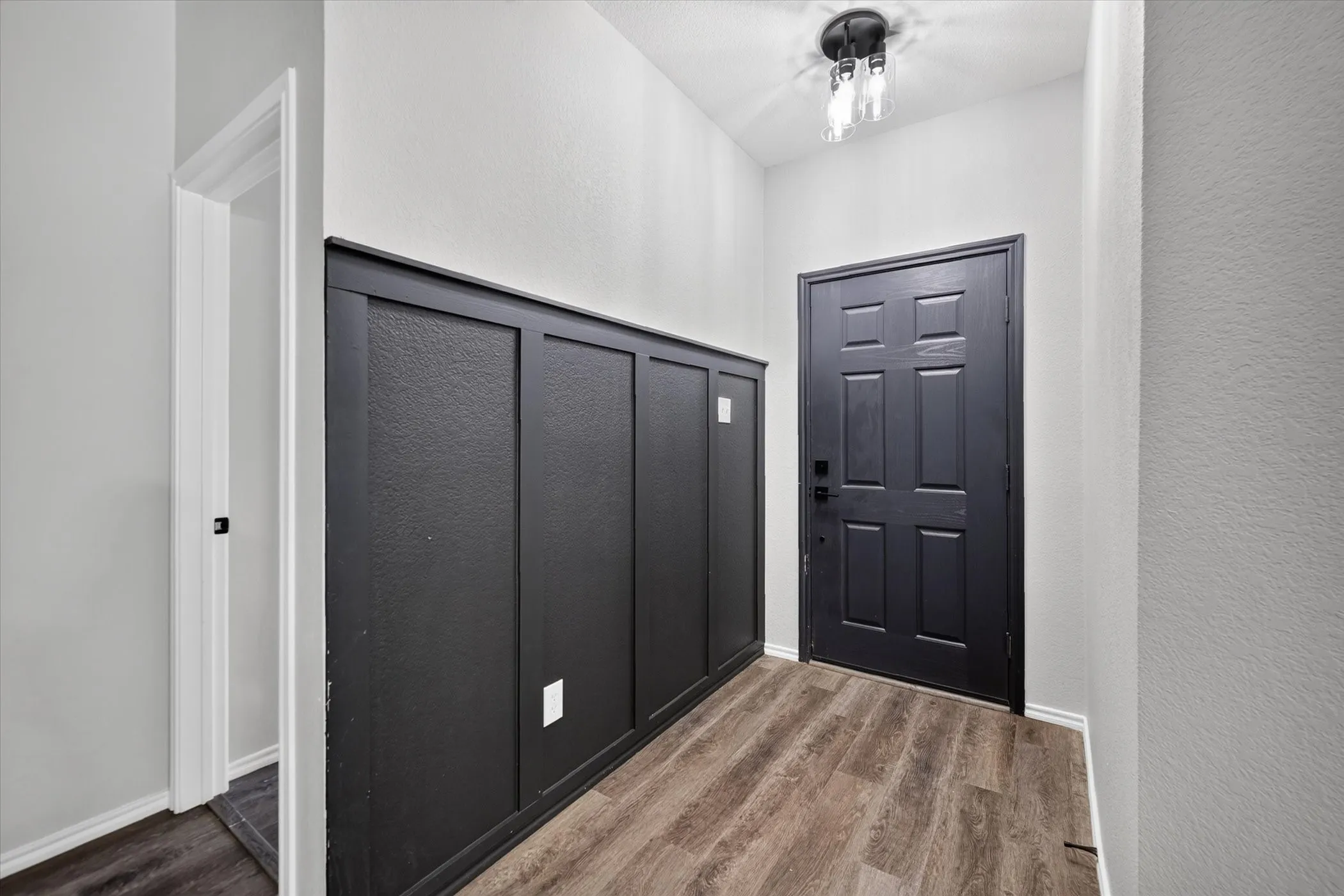 Hallway featuring smooth wood-finish flooring, white walls with clean trim detailing, and multiple dark six-panel doors with brushed nickel hardware