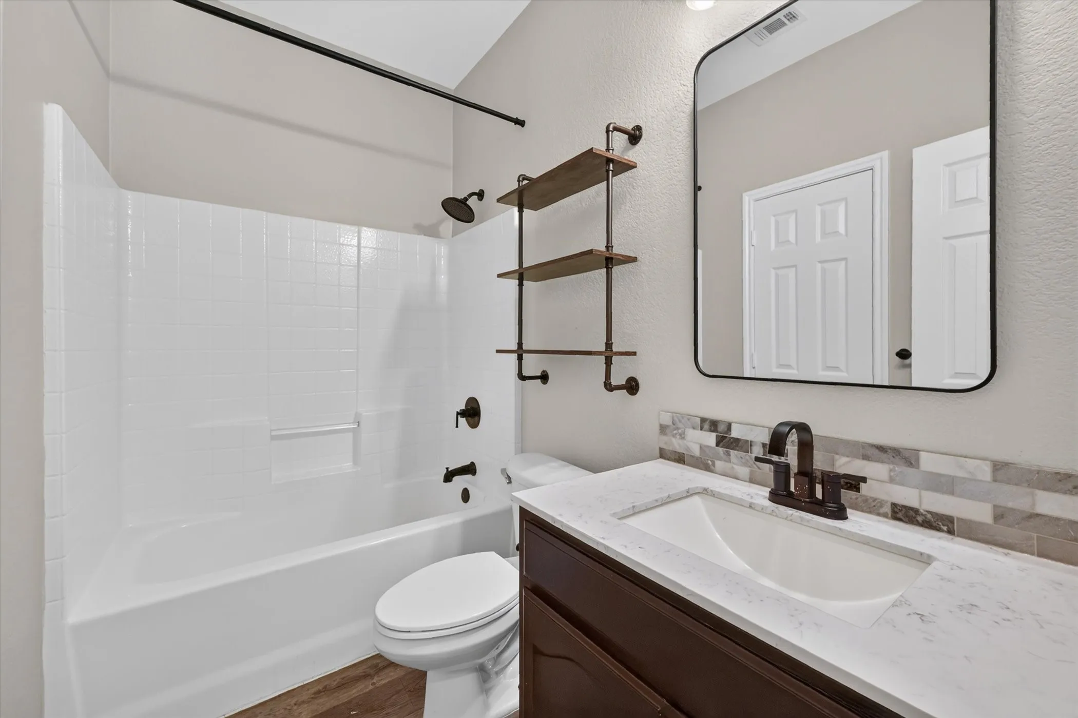 Bathroom featuring a white subway tile tub surround, wood-finish flooring, dark wood-tone vanity, white countertop, and mosaic tile backsplash