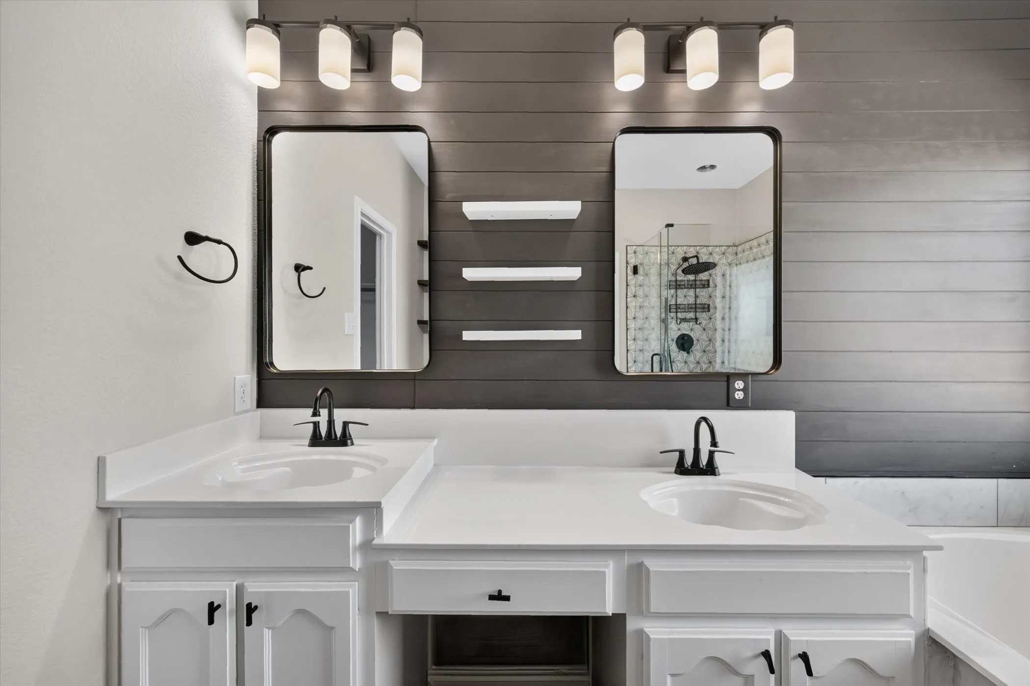 Dual vanities with integrated sinks, white countertops, dark wood-finish plank wall, wall-mounted light fixtures, and matte black hardware