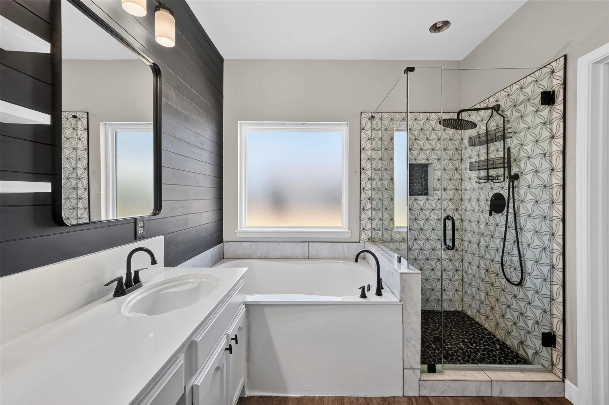Spacious bathroom featuring a built-in soaking tub, glass-enclosed shower with custom tile, vanity with undermount sink, and wood-finish flooring