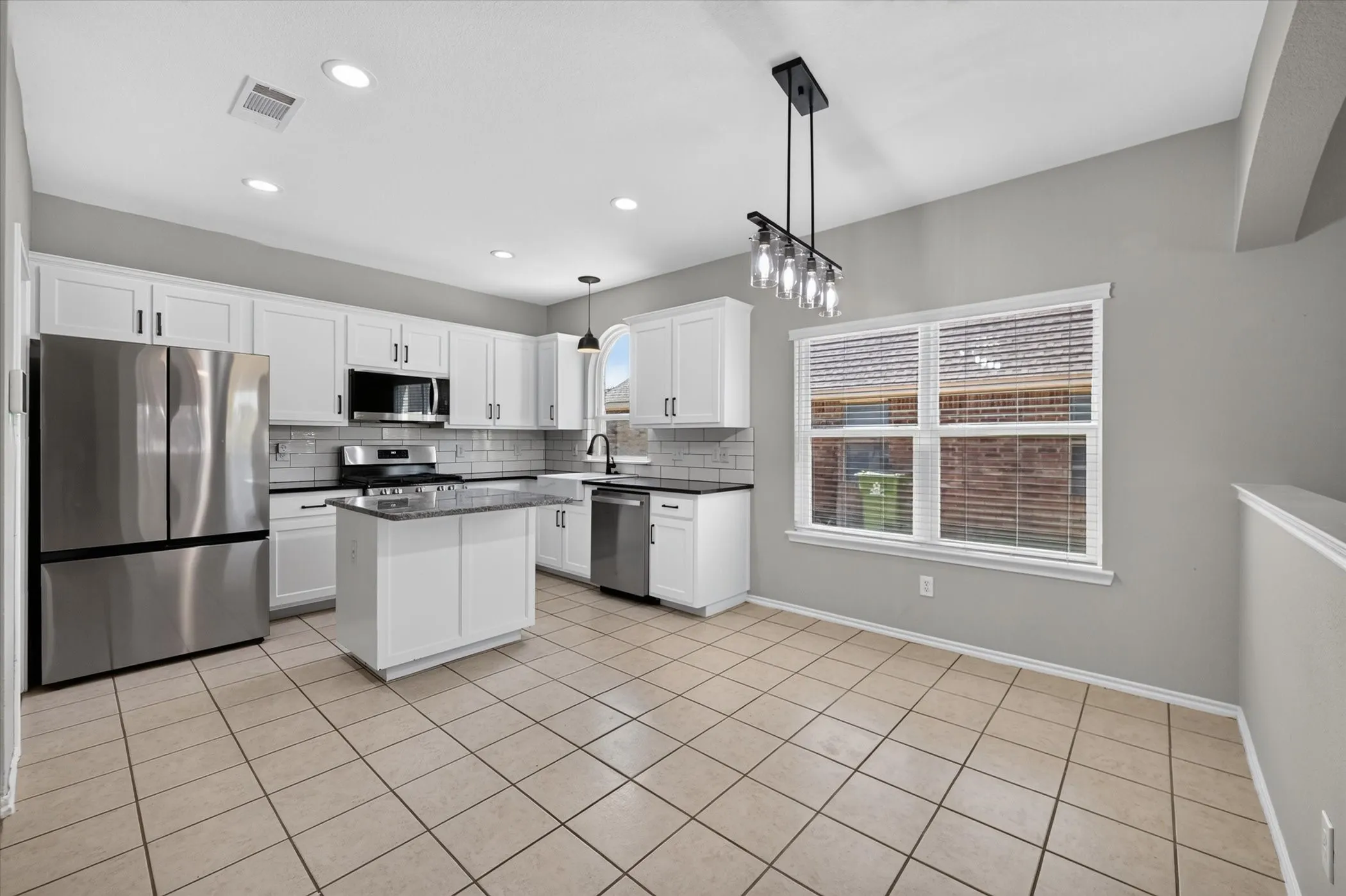 Kitchen featuring white cabinetry, a center island, stainless steel appliances, tile flooring, and a window with blinds