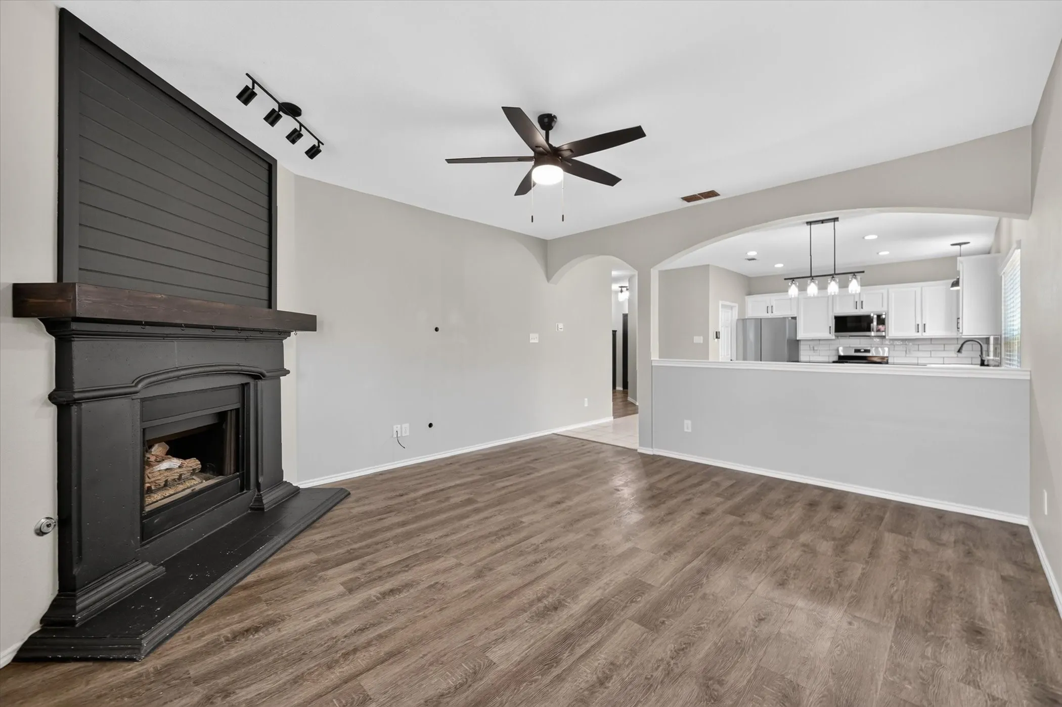 Wood-finish flooring, fireplace with dark mantel, ceiling fan, arched entryway, and recessed lighting