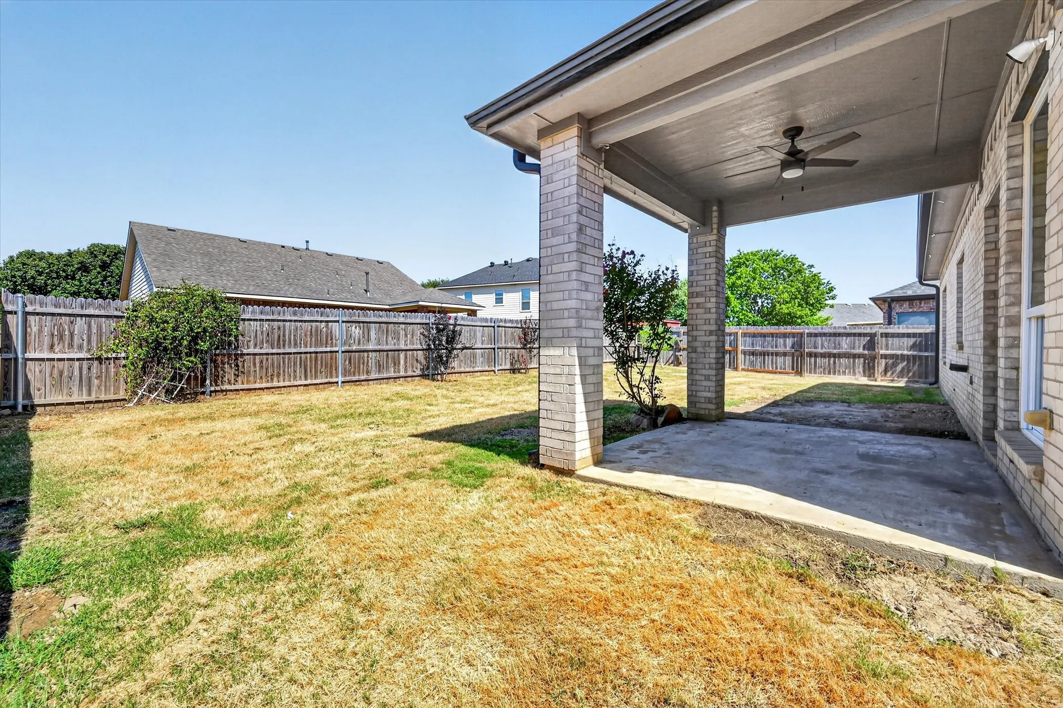 Covered patio with a ceiling fan, brick columns, and a concrete slab