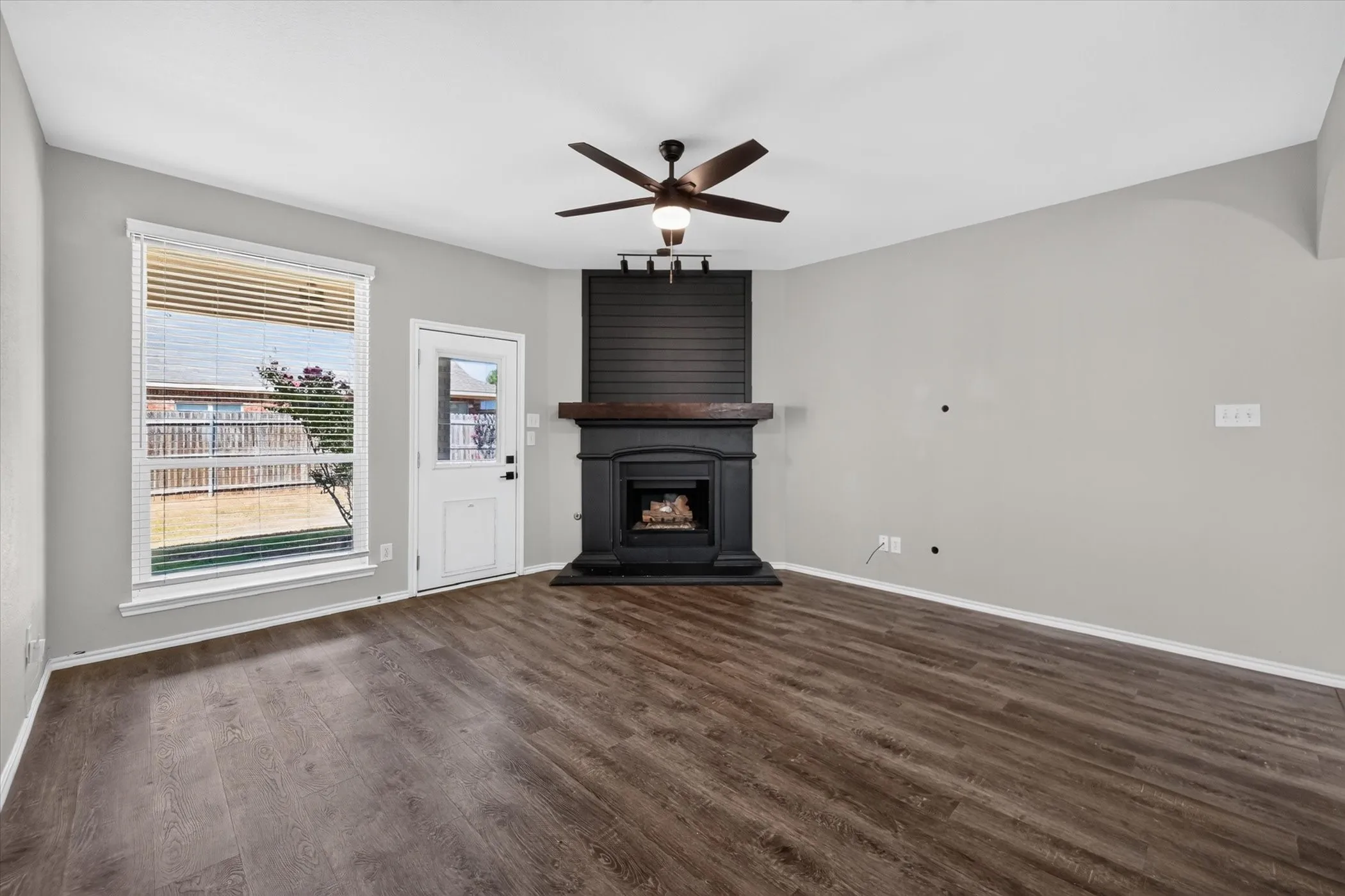 Spacious living area featuring wood-finish flooring, a black wood-burning stove with chimney stack, ceiling fan with brushed metal accents, and glass doors opening to exterior space