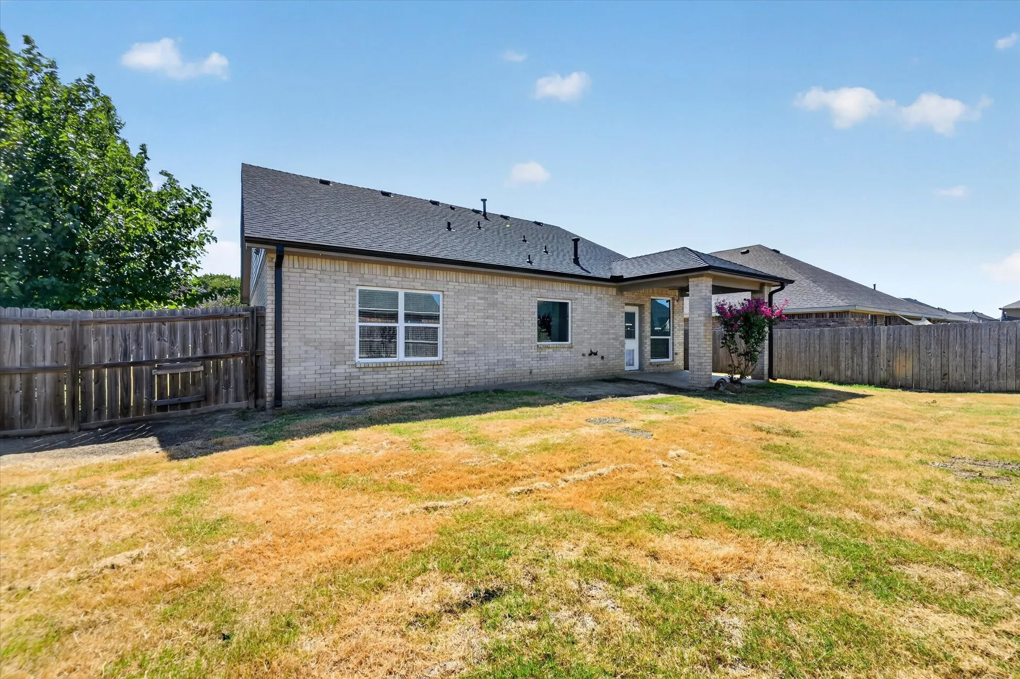 Brick exterior, covered patio, fenced yard, and a shingled roof