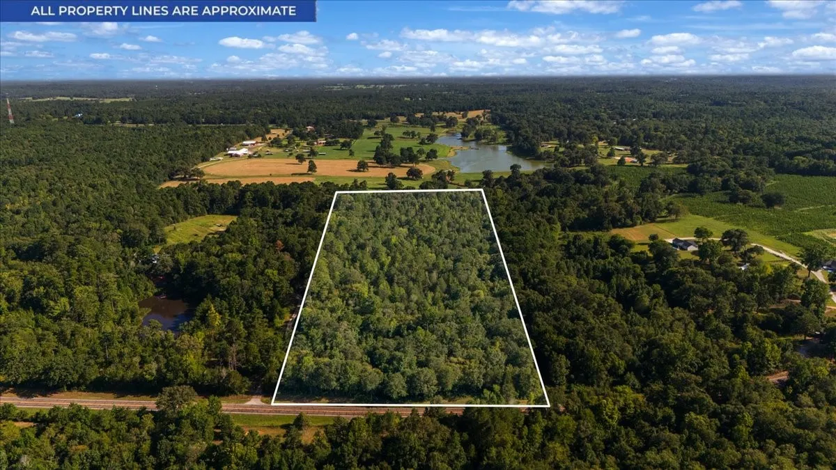 Expansive wooded land parcel, bordered by a rail line, with a distant lake and open fields