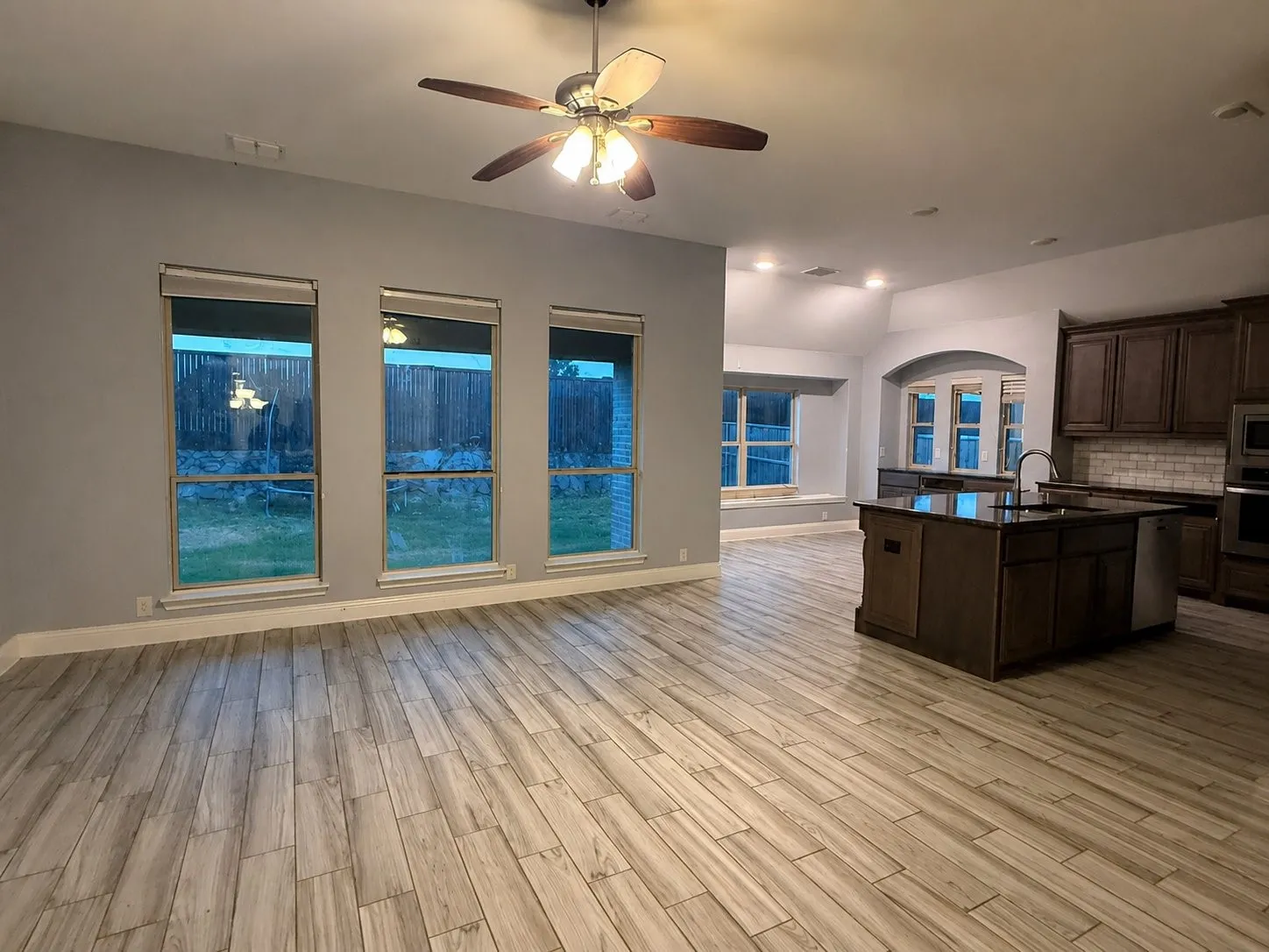 Wood-look tile flooring throughout, dark wood-finish cabinetry, kitchen island with sink, subway tile backsplash, and recessed lighting