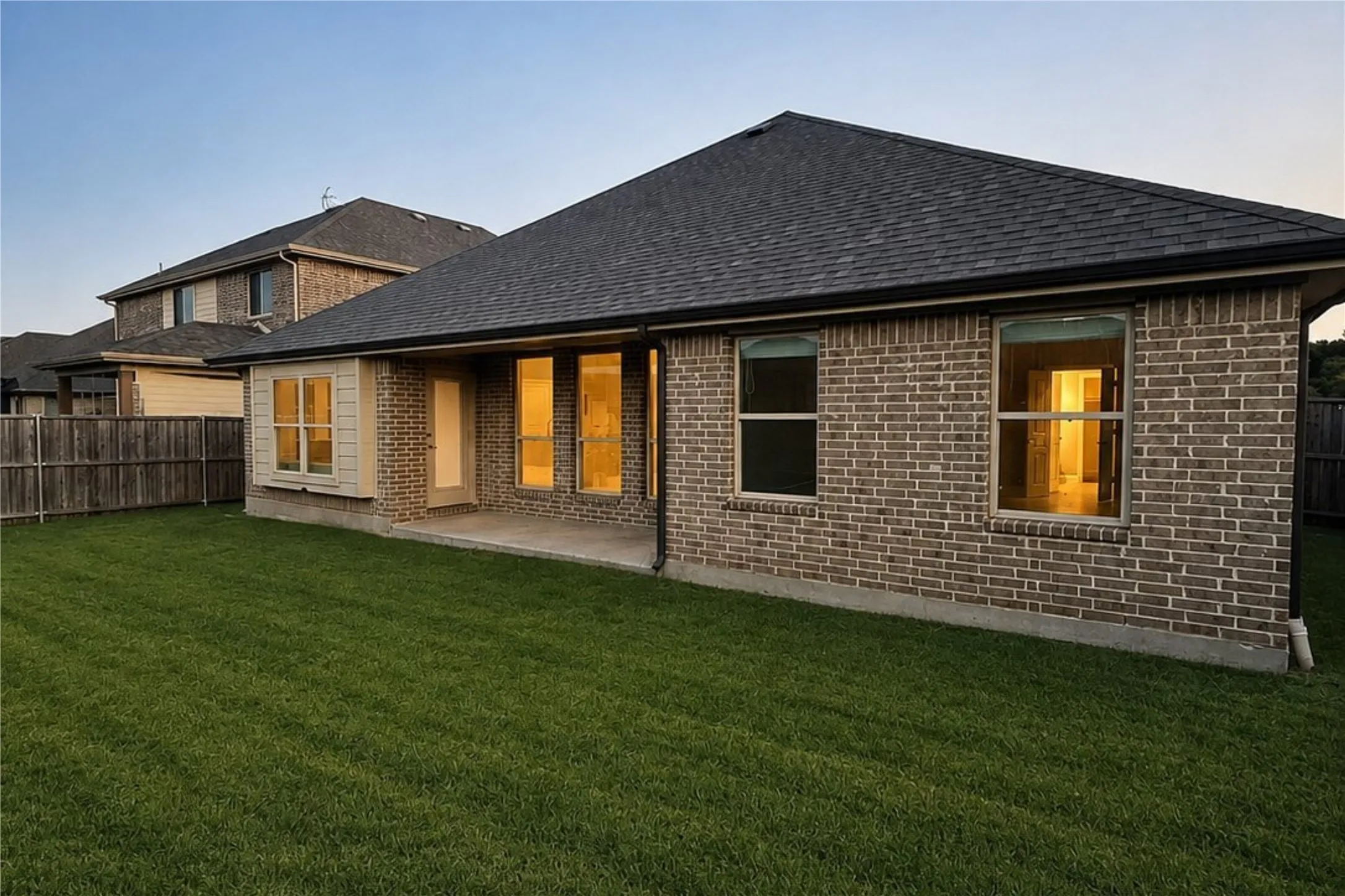 Brick exterior with contemporary architectural lines, expansive rear patio with concrete foundation, multiple glass door and window openings flooding interior spaces with natural light, manicured lawn, and coordinating two-story residence visible in background