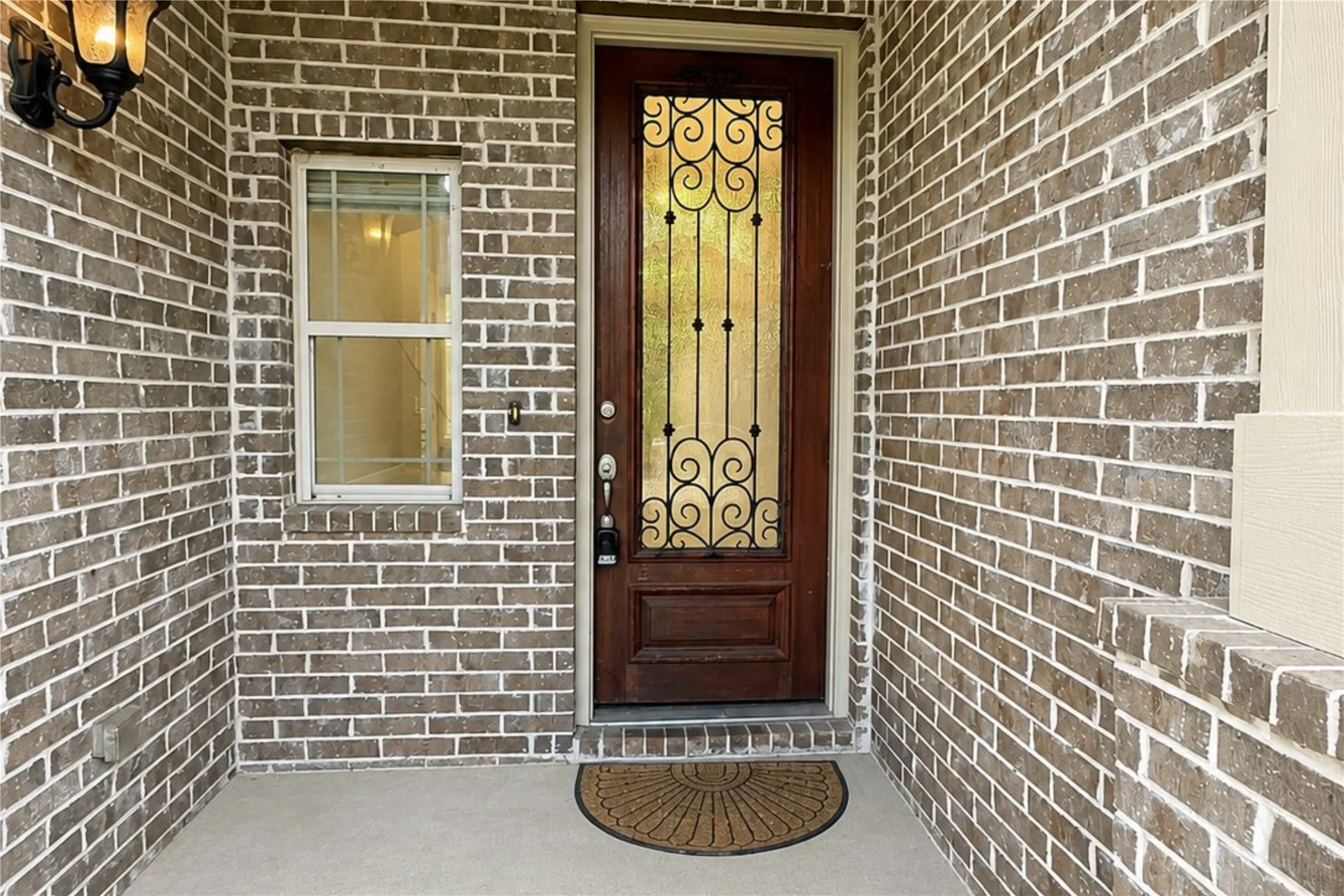 Brick exterior facade with a dark wood entry door featuring decorative wrought iron and glass