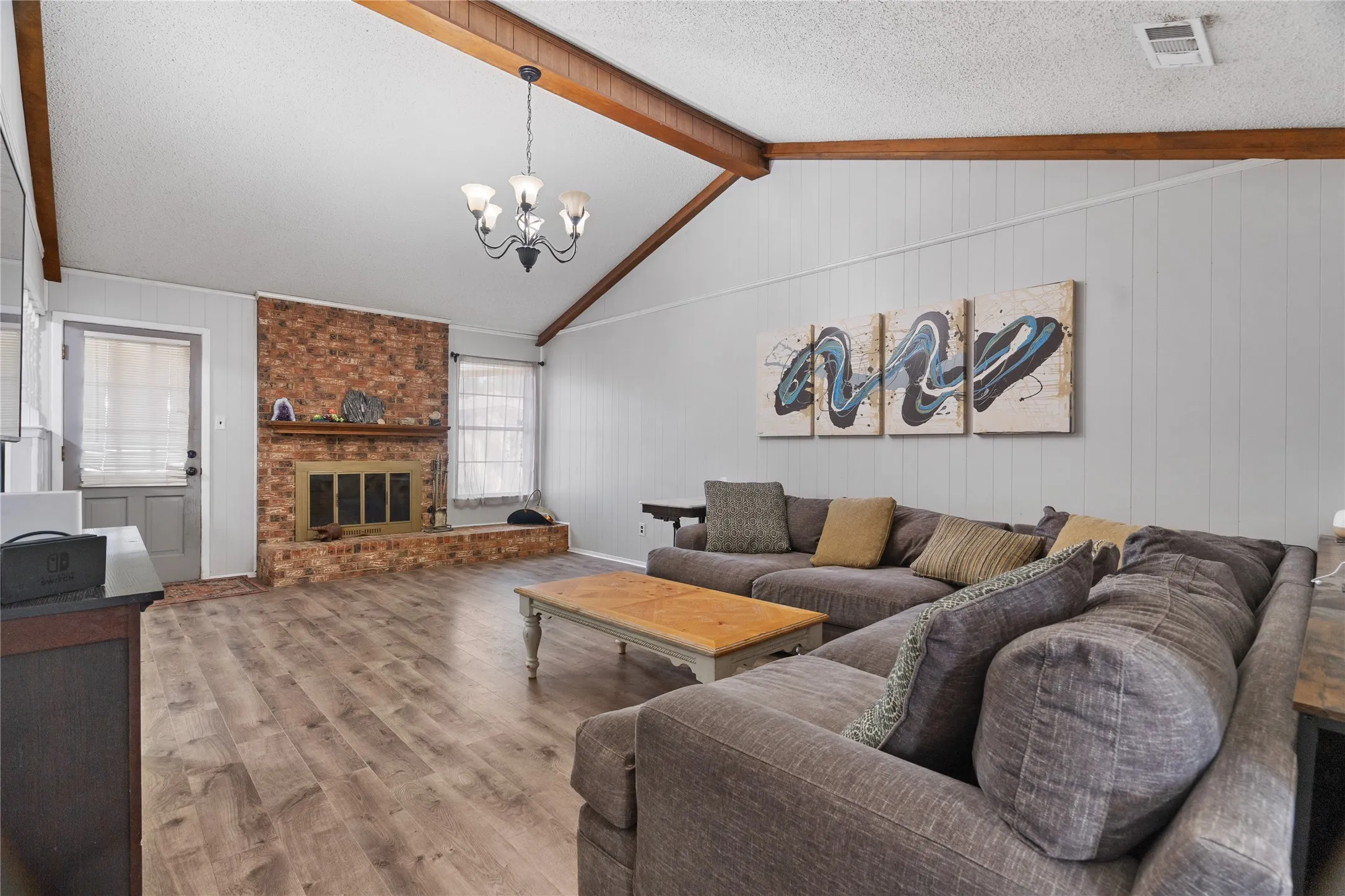 Large family room with beamed high ceilings, brick wood burning fireplace, and door to back covered patio.