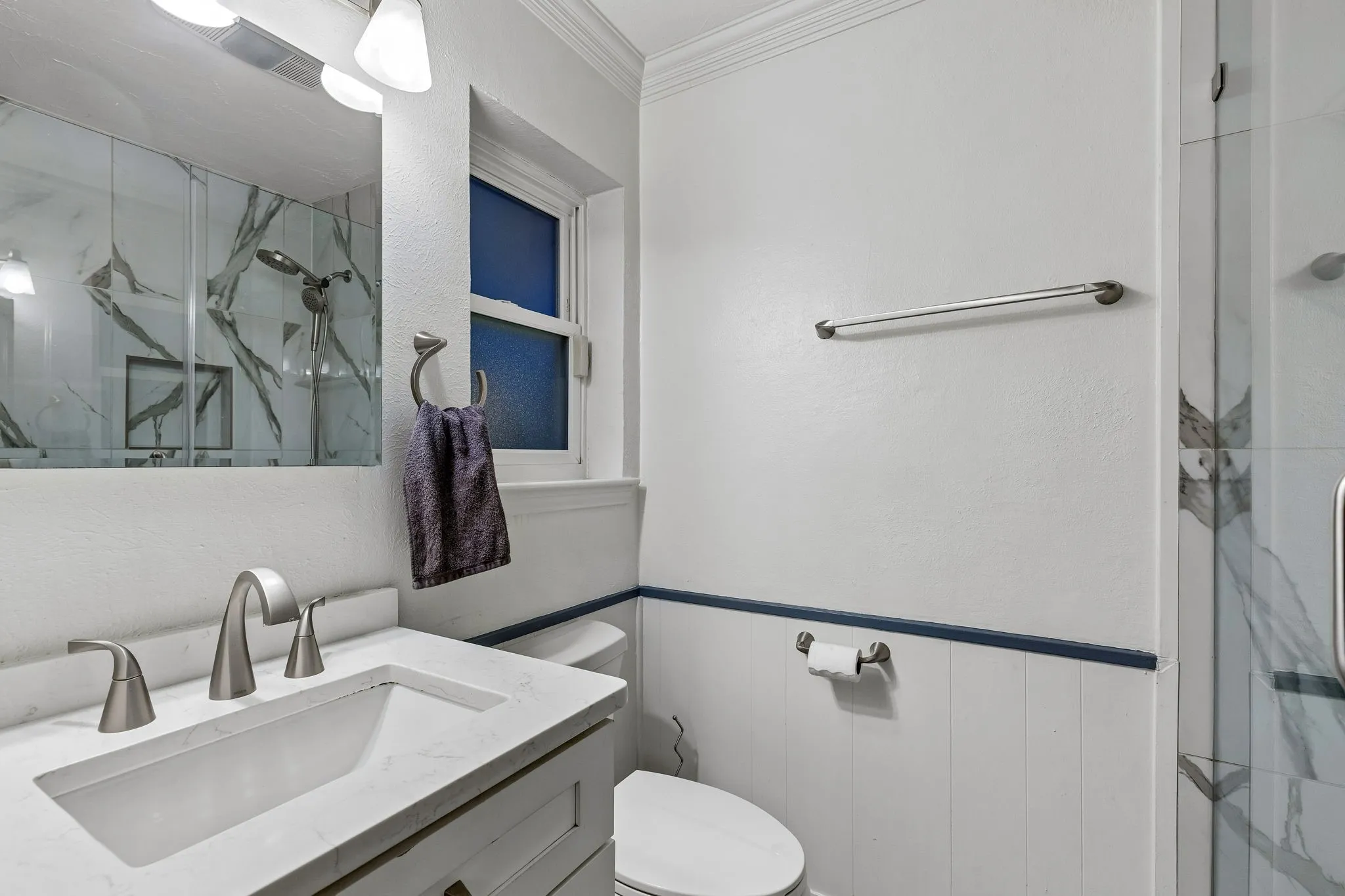 Bathroom featuring a marble finish shower, vanity, ornamental molding, and a wainscoted wall