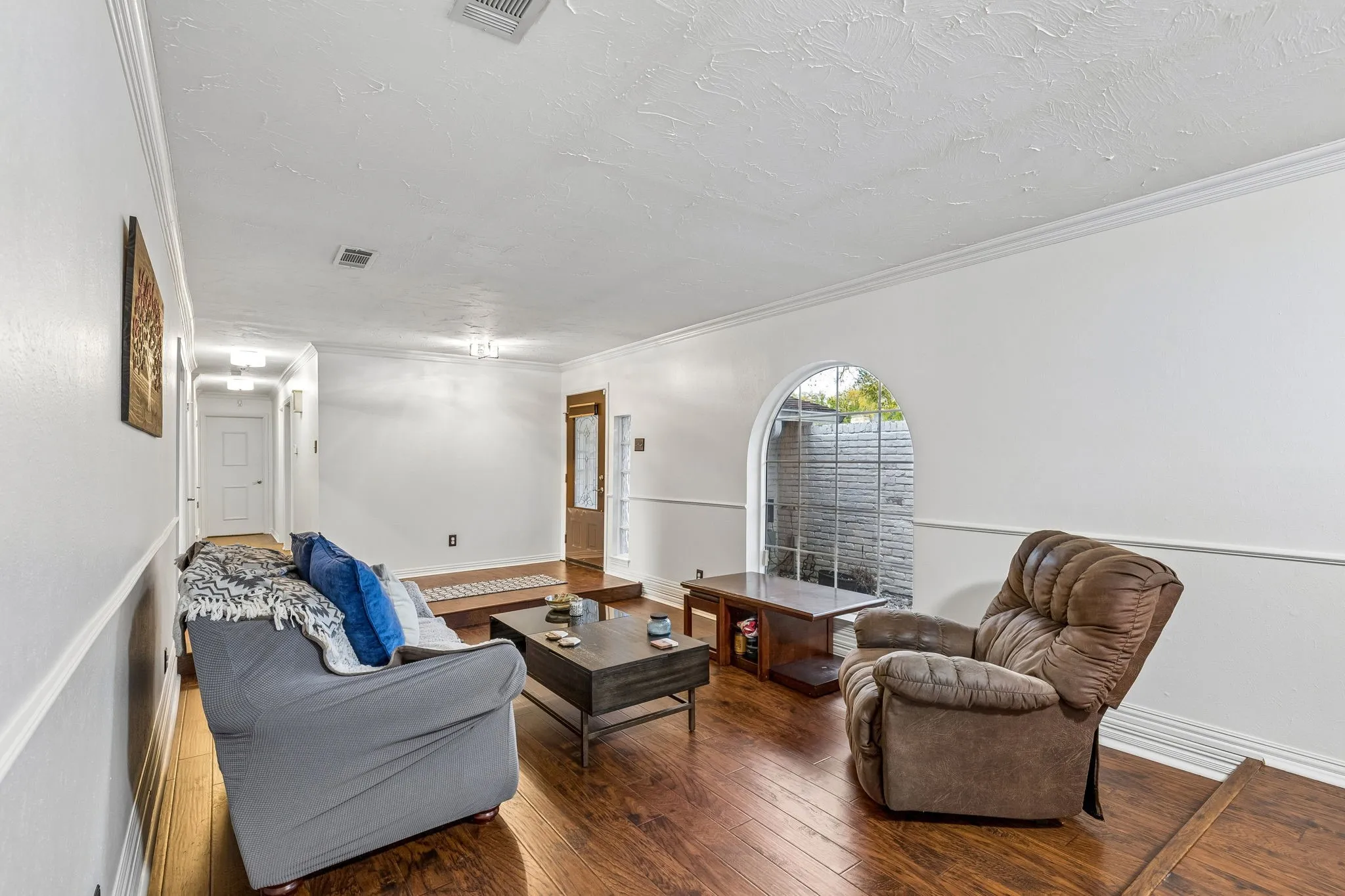 Living area with wood-type flooring, ornamental molding, and a textured ceiling