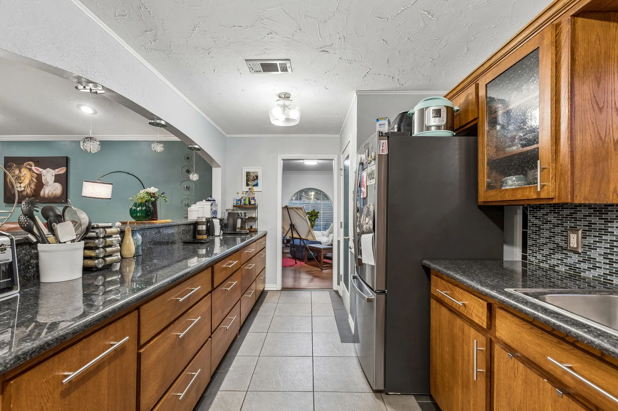 Kitchen featuring wood finish cabinetry, light tile patterned floors, stainless steel fridge with ice dispenser, glass fronted cabinets, and crown molding