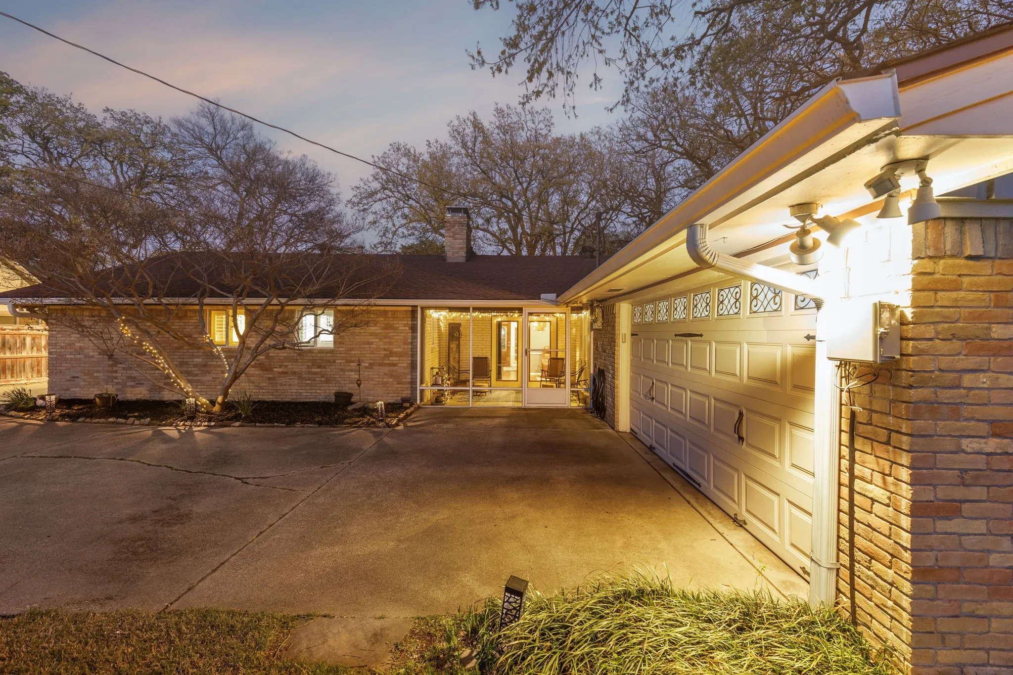 Property exterior at dusk featuring a chimney, brick siding, an attached garage, a patio, and driveway