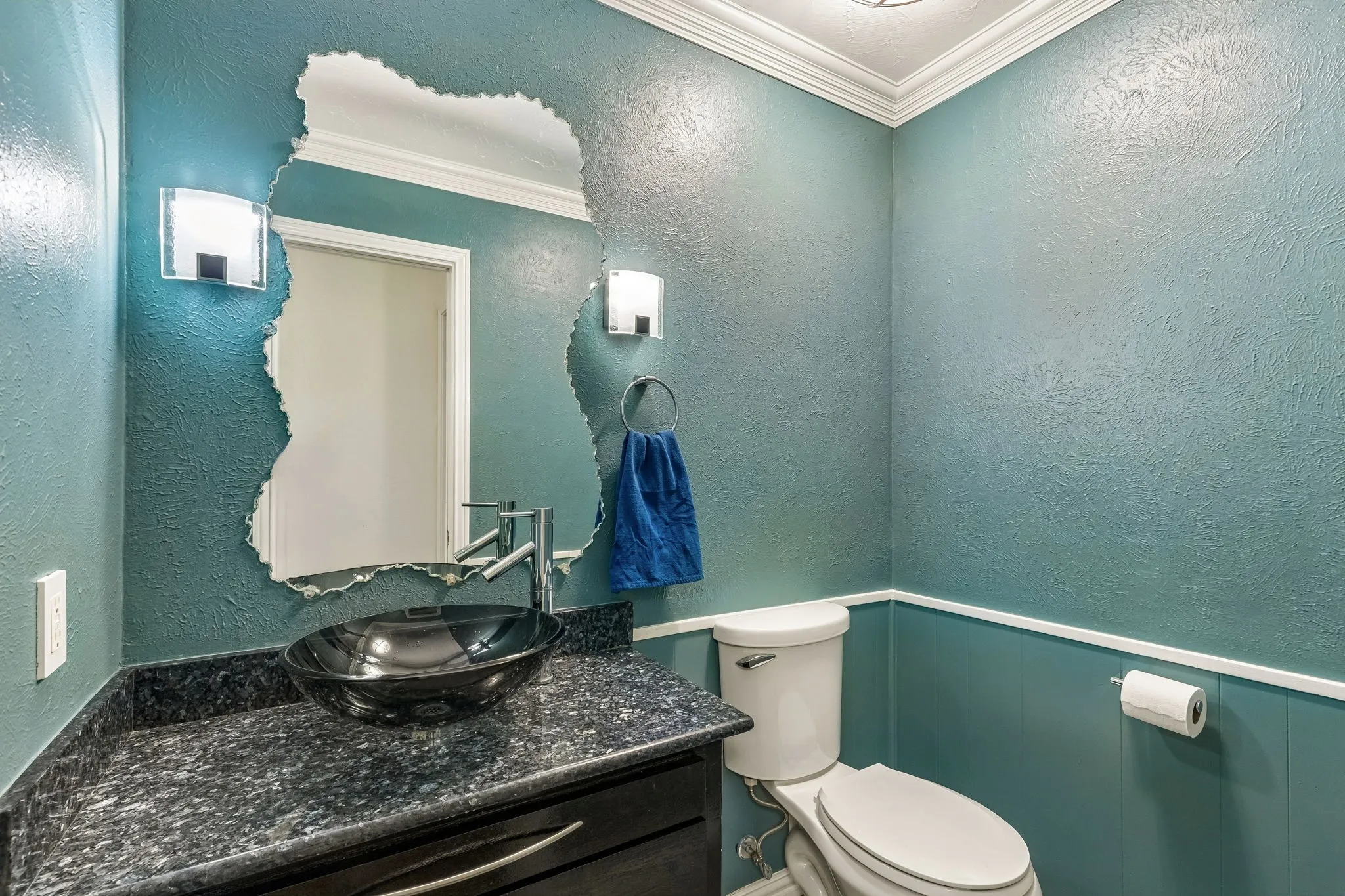 Half bathroom featuring a textured wall, ornamental molding, vanity, and wainscoting