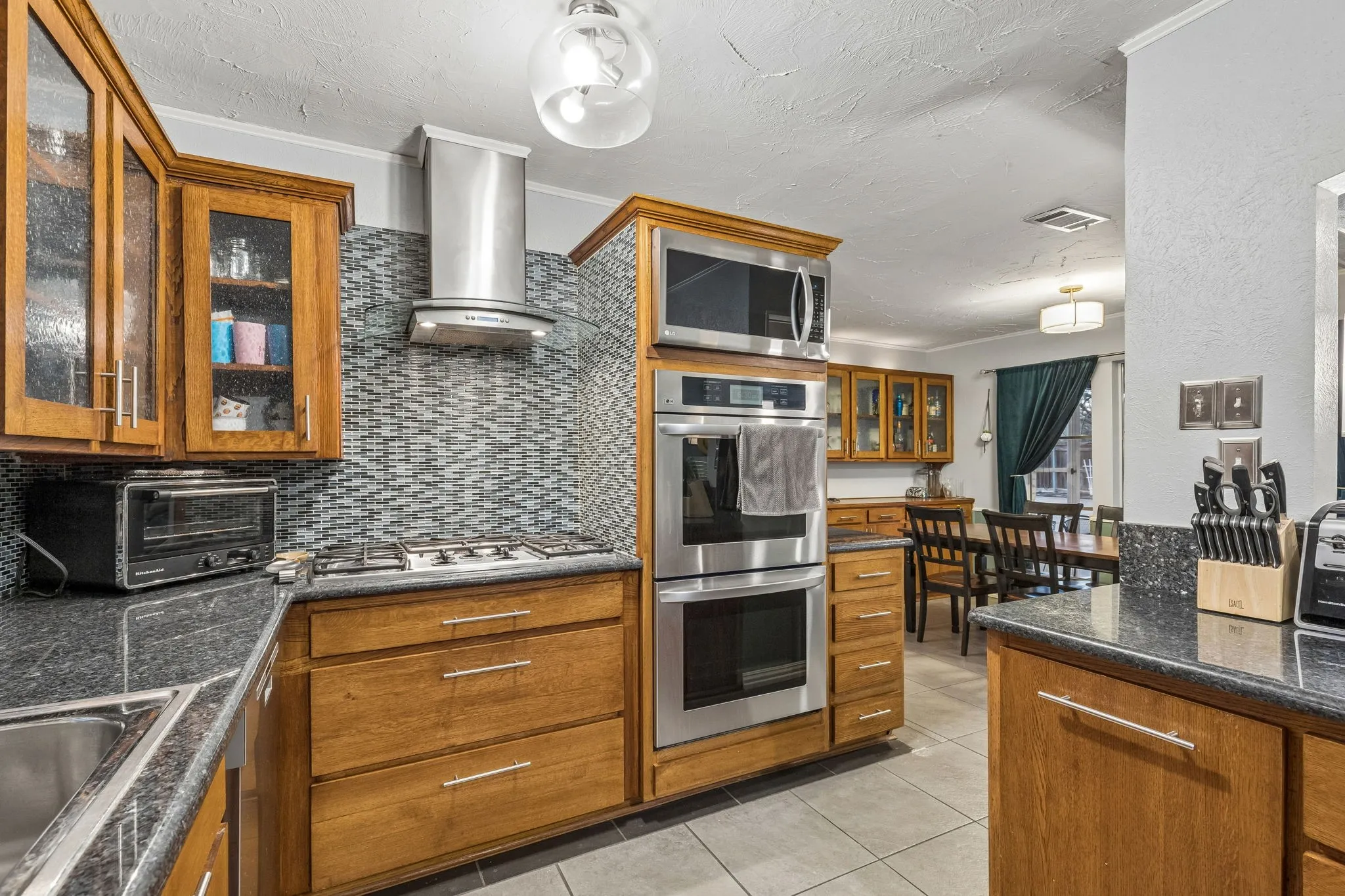 Kitchen with glass fronted cabinets, wood finish cabinets, stainless steel appliances, dark stone counters, and a textured ceiling