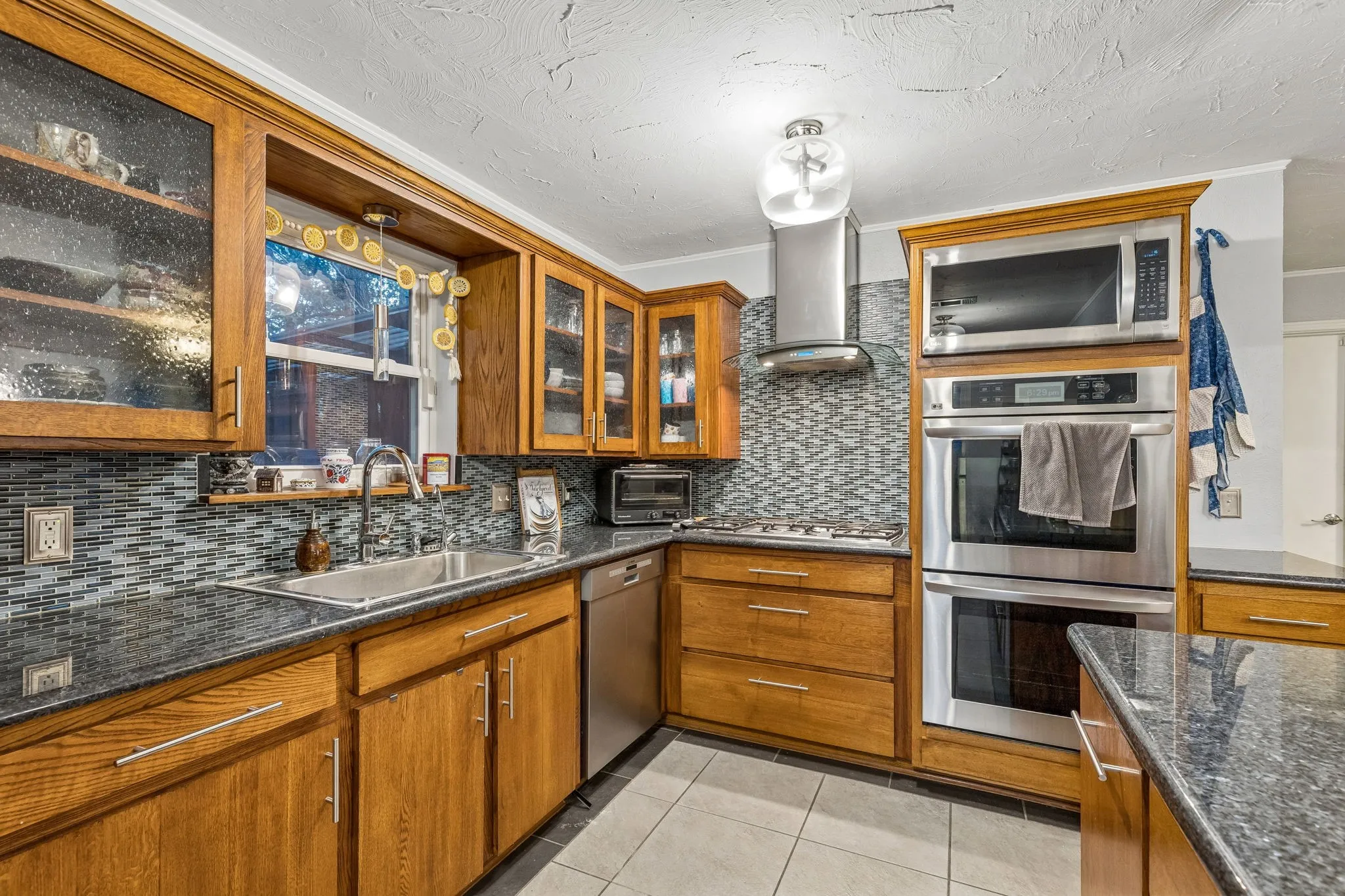 Kitchen with wood finish cabinetry, light tile patterned flooring, stainless steel appliances, dark stone countertops, and a textured ceiling