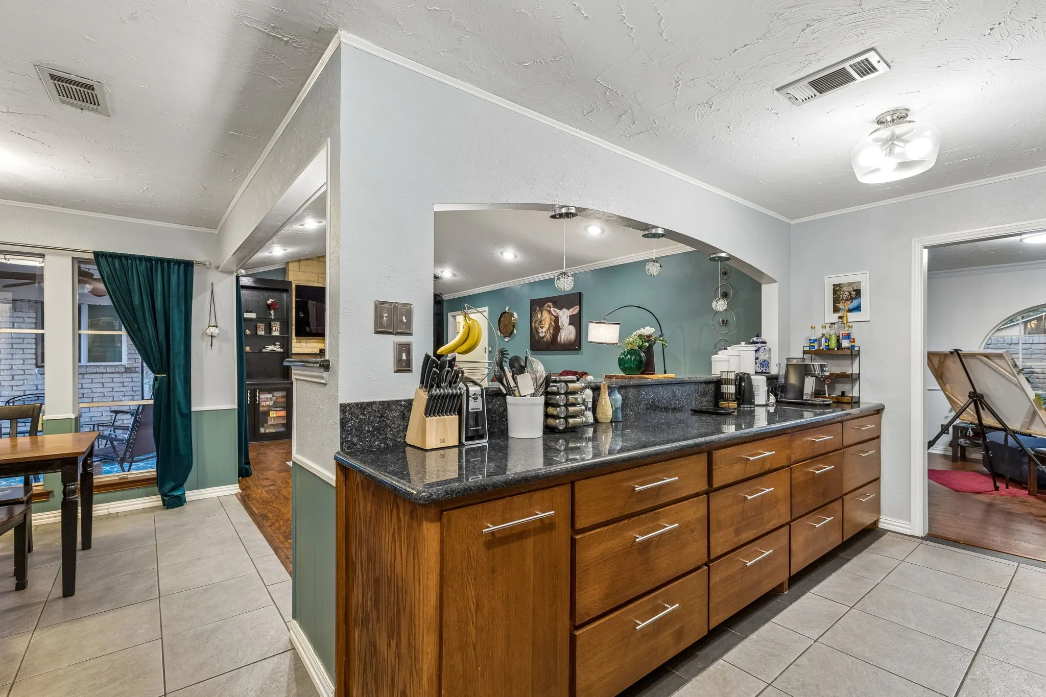 Kitchen featuring light tile patterned floors, ornamental molding, dark stone counters, wood finish cabinets, and wainscoting