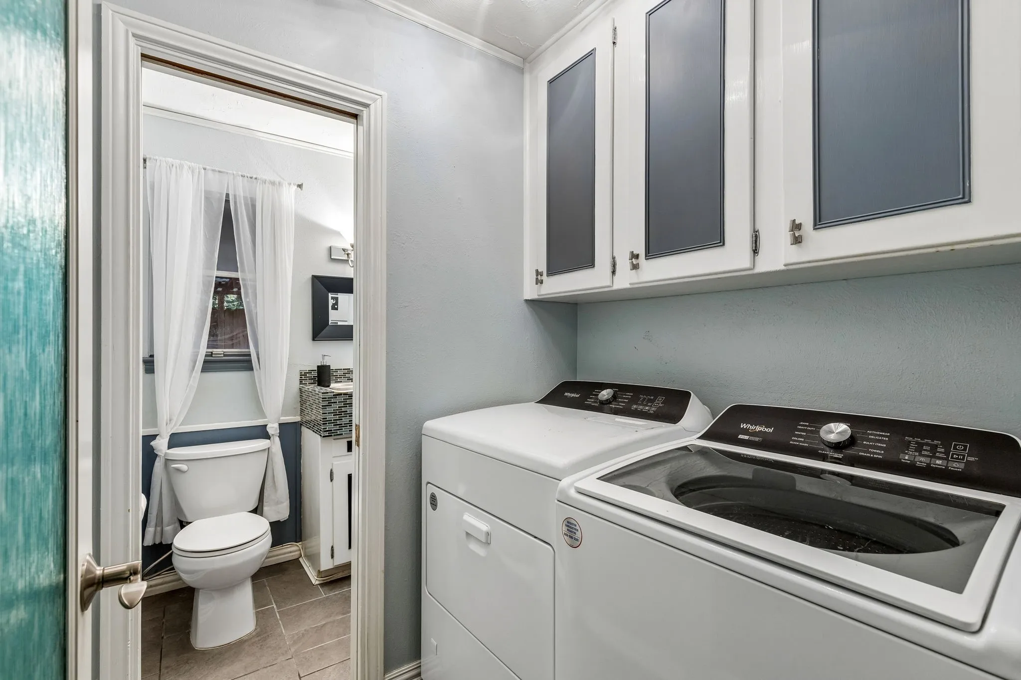 Laundry area featuring light tile patterned floors, separate washer and dryer, and cabinet space