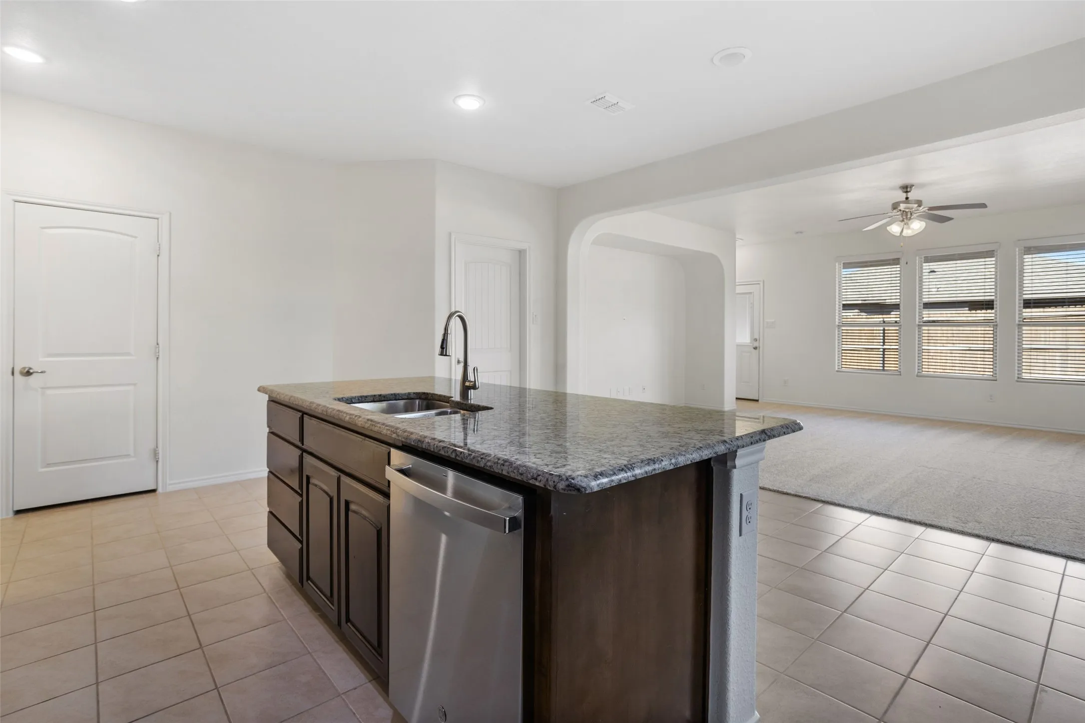 Kitchen with ceiling fan, sink, dishwasher, light tile flooring, and an island with sink