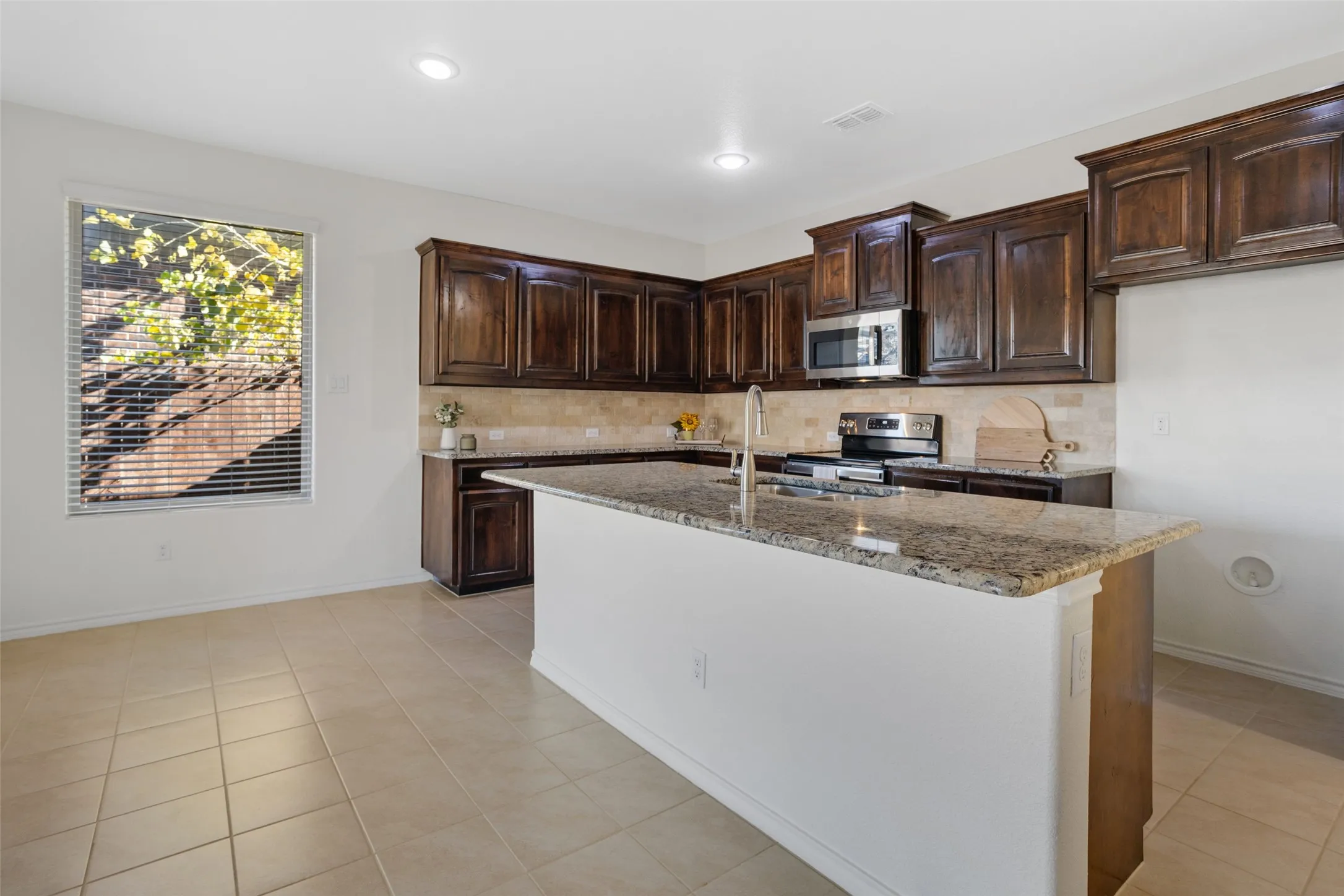 Kitchen featuring appliances with stainless steel finishes, dark brown cabinets, light stone countertops, and light tile flooring