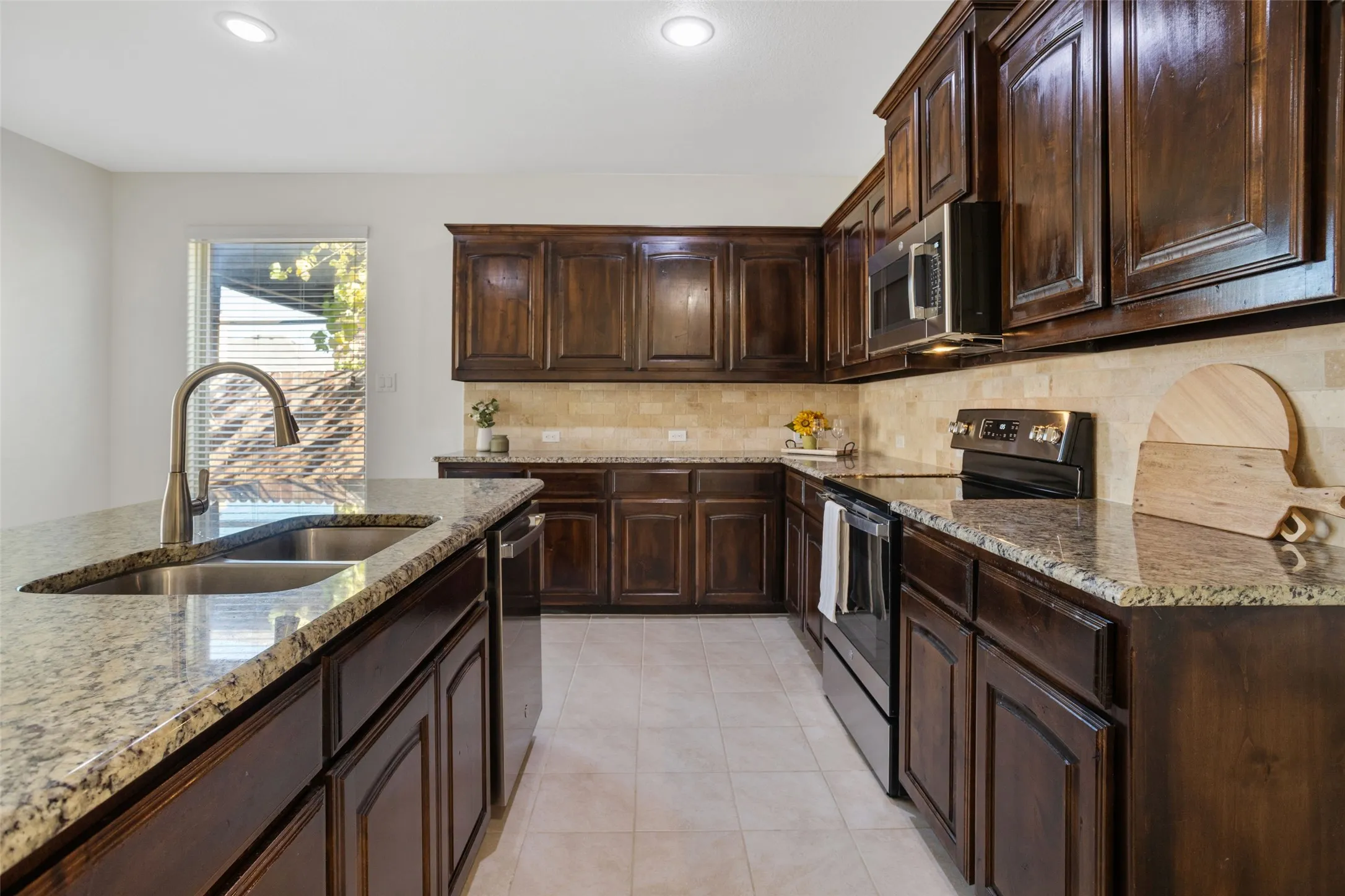 Kitchen featuring light tile flooring, dark brown cabinets, stainless steel appliances, sink, and light stone counters