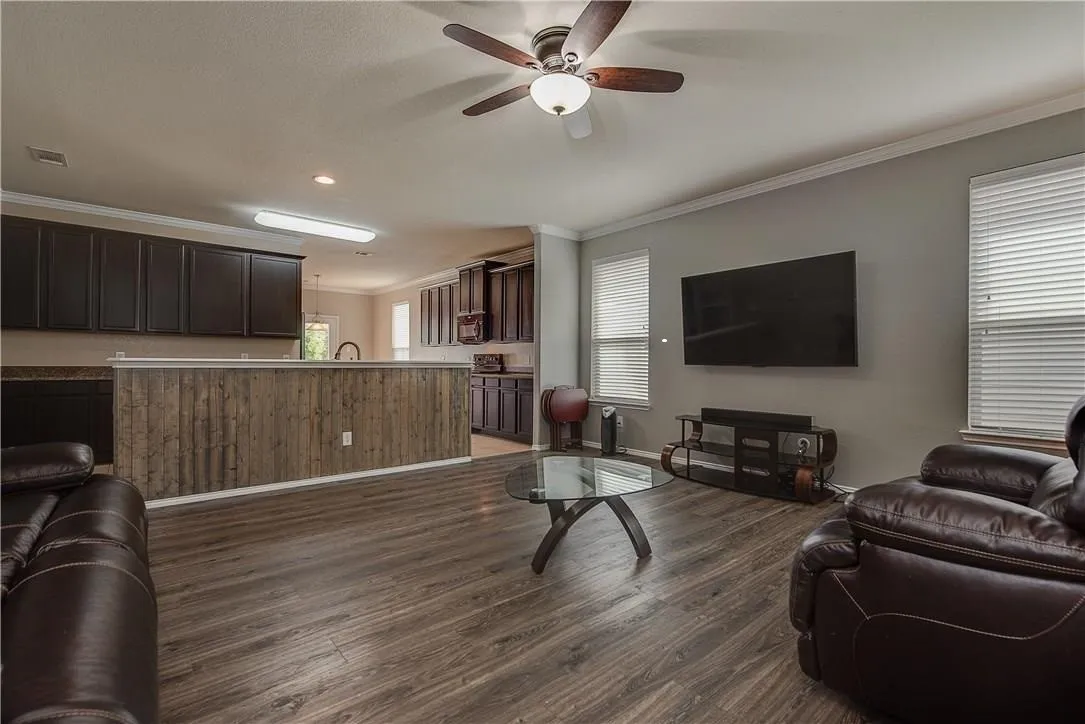 STAGED - Spacious living area featuring wood-finish flooring, ceiling fan, light gray walls, and white crown molding. Open to Kitchen.