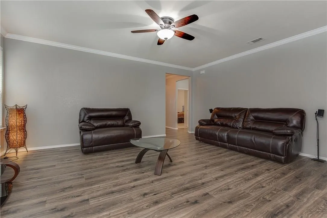 STAGED - Spacious living area featuring wood-finish flooring, ceiling fan, light gray walls, and white crown molding. Open to Kitchen.