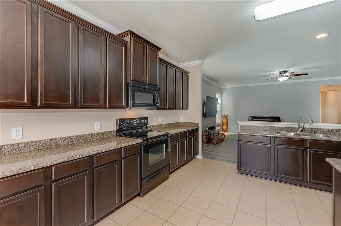STAGED - Kitchen featuring granite counters, undermount double sink, black appliances: dishwasher, glass-top range, microwave & refrigerator.