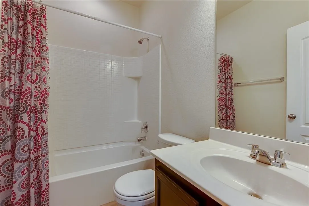 STAGED - Bathroom featuring a white tub/shower combination with a textured tile surround, a built-in shower caddy, and chrome faucets.