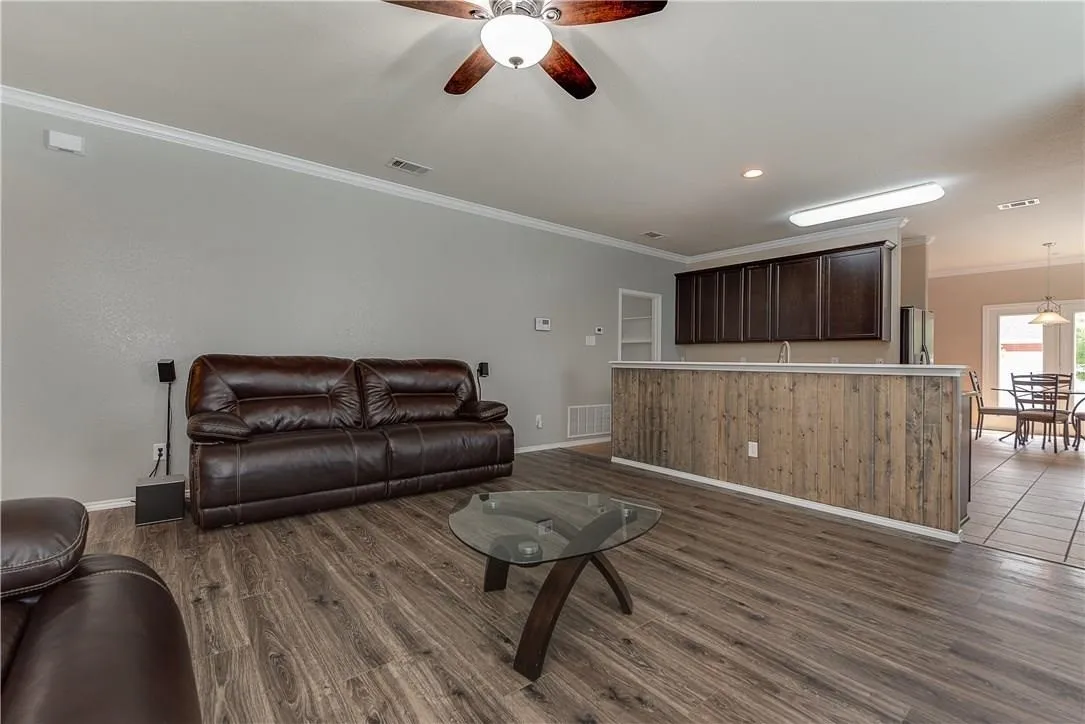 STAGED - Spacious living area featuring wood-finish flooring, ceiling fan, light gray walls, and white crown molding. Open to Kitchen.