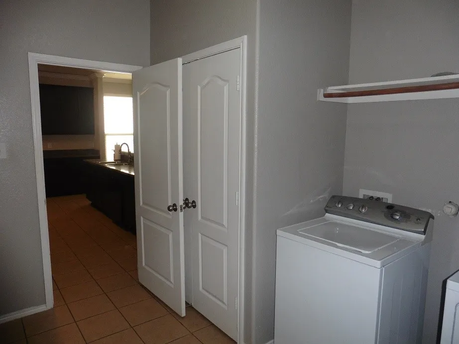 Kitchen Pantry and Utility combo room features Full-Sized Washer and Dryer, drip dry hanging area, neutral tile flooring, built-in shelving, light-toned walls, and access to the water heater and furnace closet.