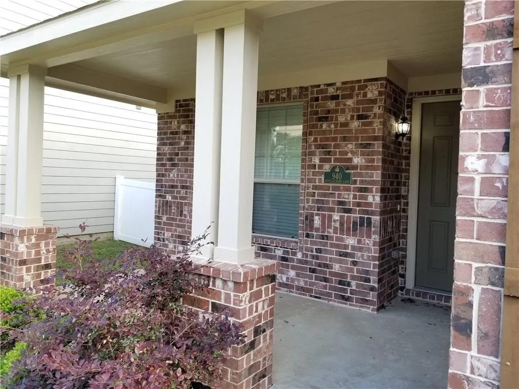 Brick facade residence featuring a covered entry porch, dark wood-finish front door, and decorative wood-finish window shutters