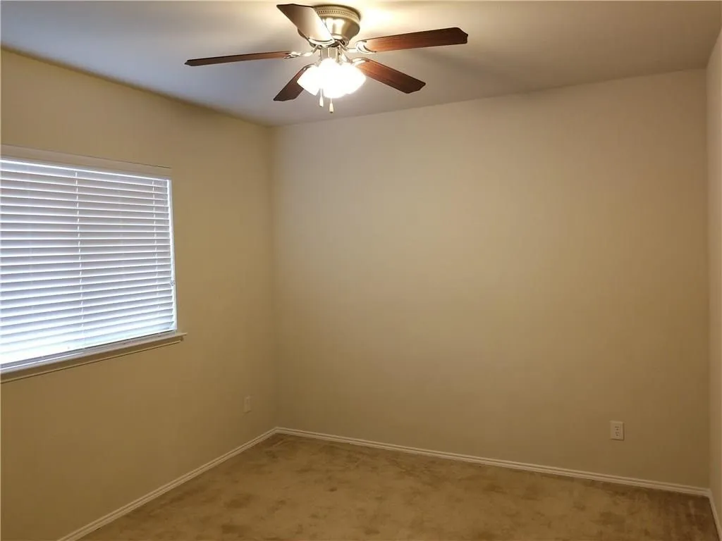 Carpeted room featuring a large window with horizontal blinds, ceiling fan, and neutral wall paint.