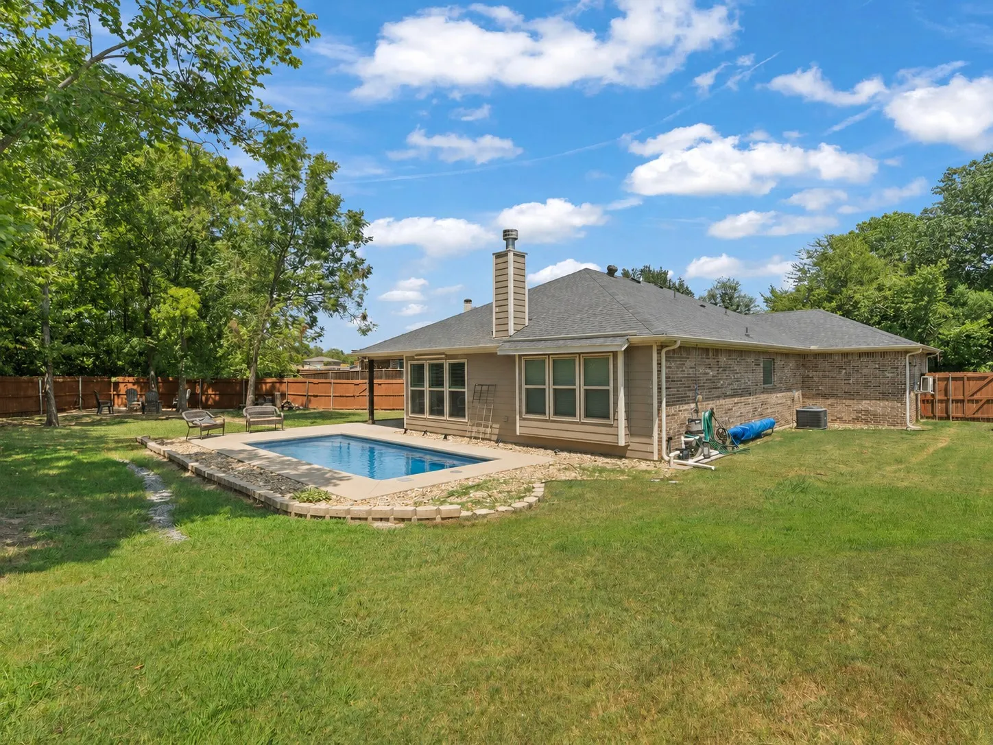 Backyard fiberglass swimming pool surrounded by a large, fenced lot with mature shade trees.