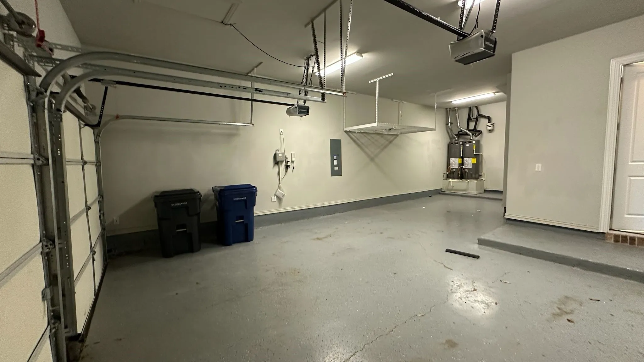 Spacious garage with epoxy-coated flooring, overhead storage racks, and two water heaters