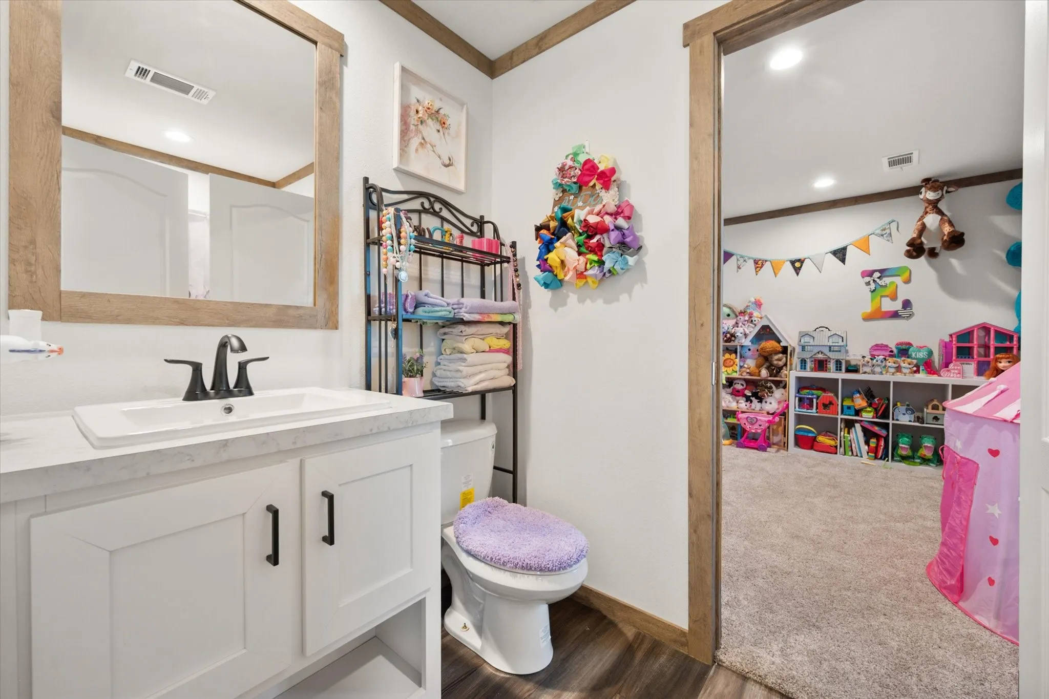 Jack and Jill Bathroom Bright, dual-sink bathroom featuring white cabinetry with black hardware, a wood-finish framed mirror, and a decorative floral wreath