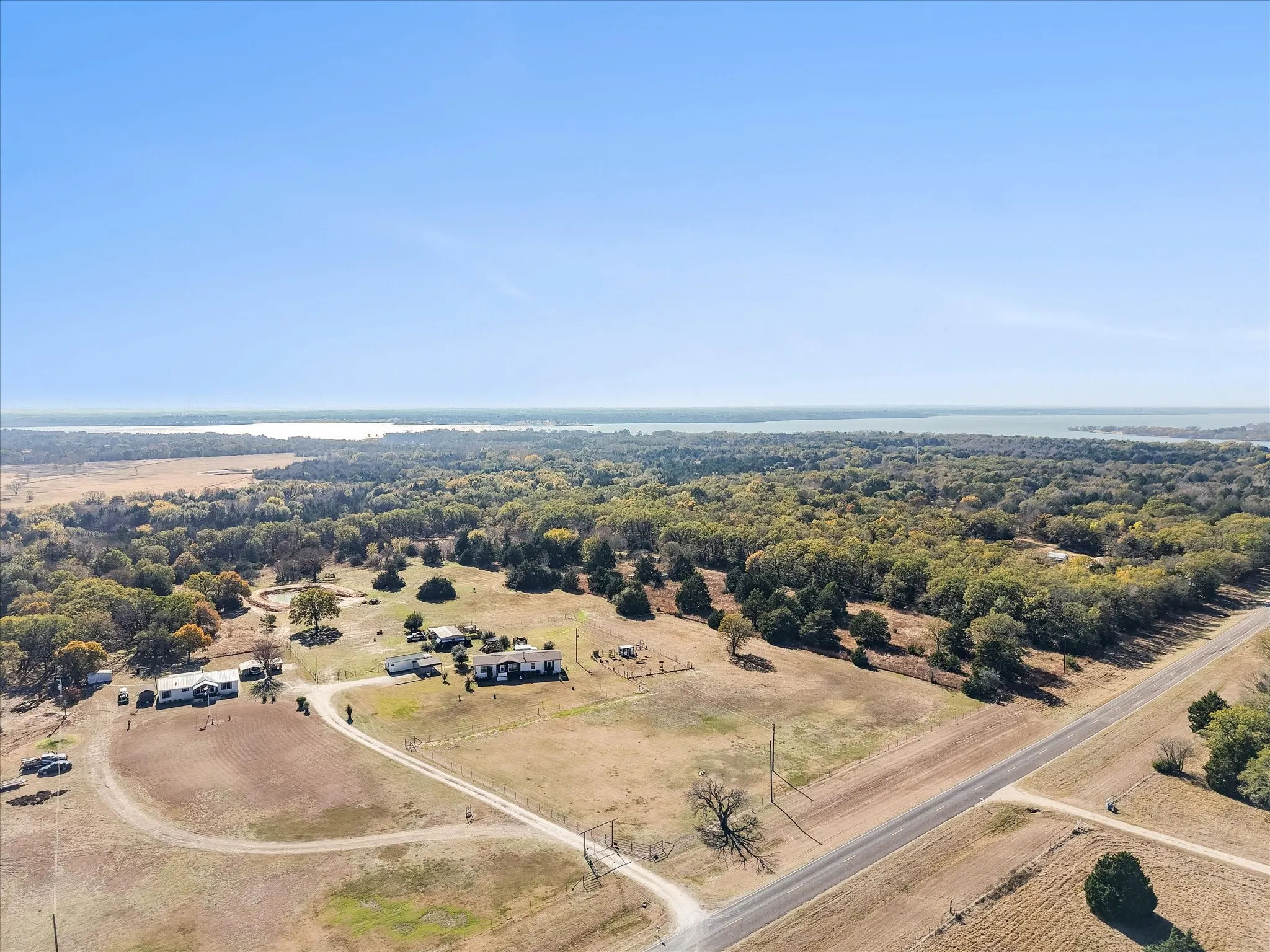Expansive rural acreage featuring a circular driveway, established tree-lined perimeter, and multiple outbuildings set on gently rolling terrain