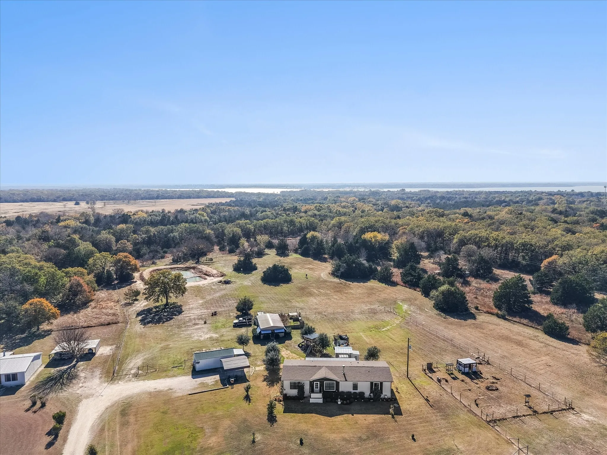 Expansive property featuring multiple structures, a pond, and surrounding mature trees