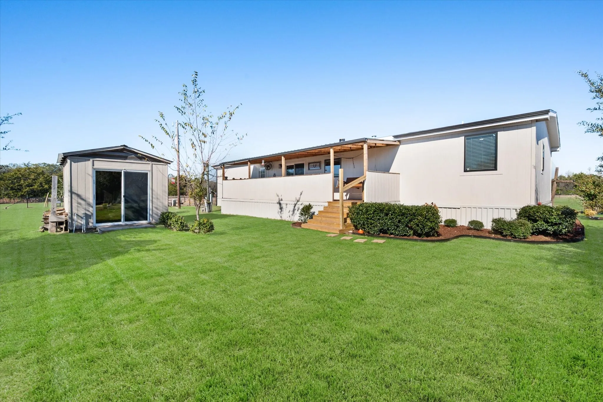 Expansive yard with green grass, a detached shed with sliding glass doors, a wood deck with stairs, and landscaped garden beds