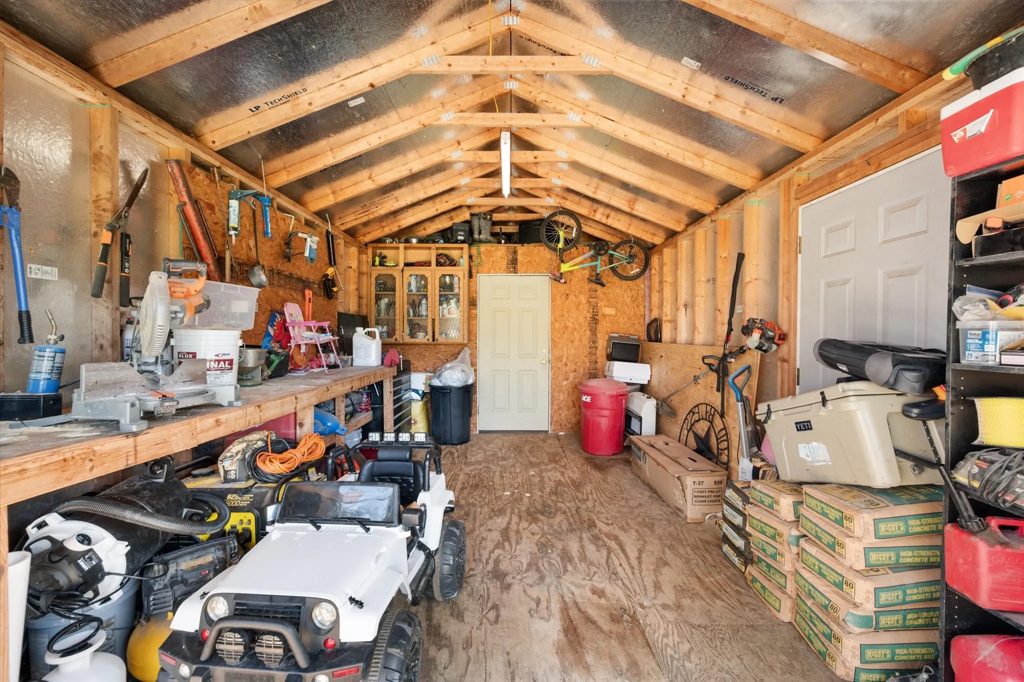 Exposed wood beam ceiling, exposed wood stud walls, built-in workbench, plywood flooring, interior doors