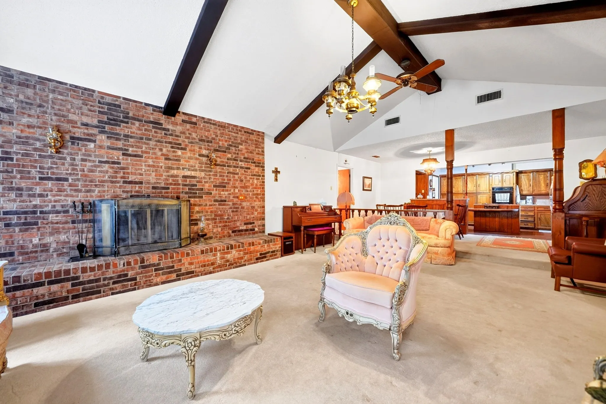 Spacious open-concept living area featuring exposed wood beam ceiling details, brick fireplace with glass doors, wood-finish flooring throughout, and abundant natural light from skylights and clerestory windows