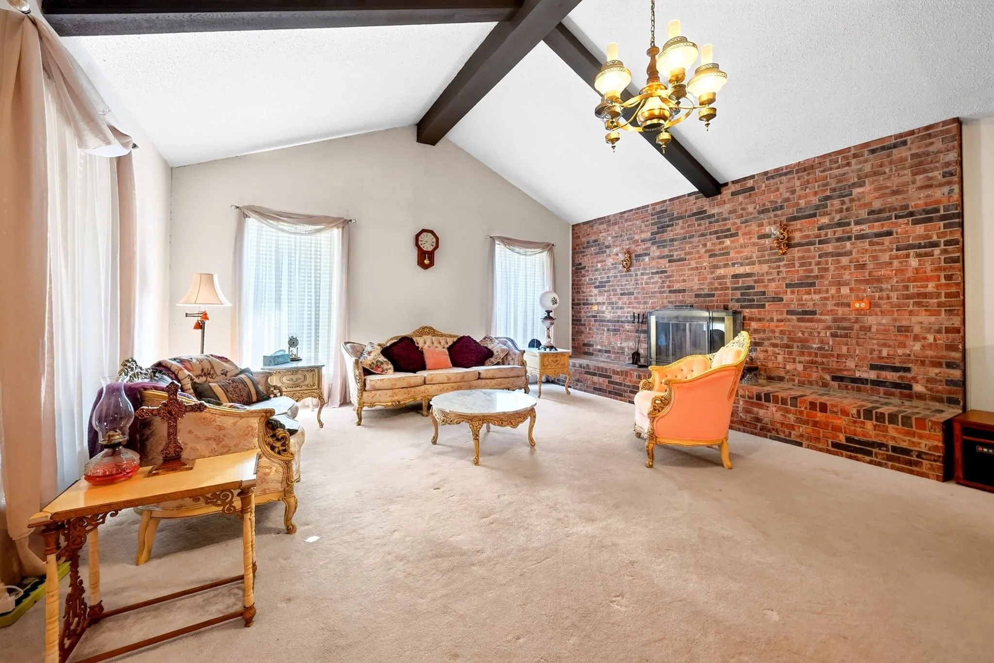 Vaulted ceiling with exposed beams, brick accent wall with fireplace, and a hanging chandelier