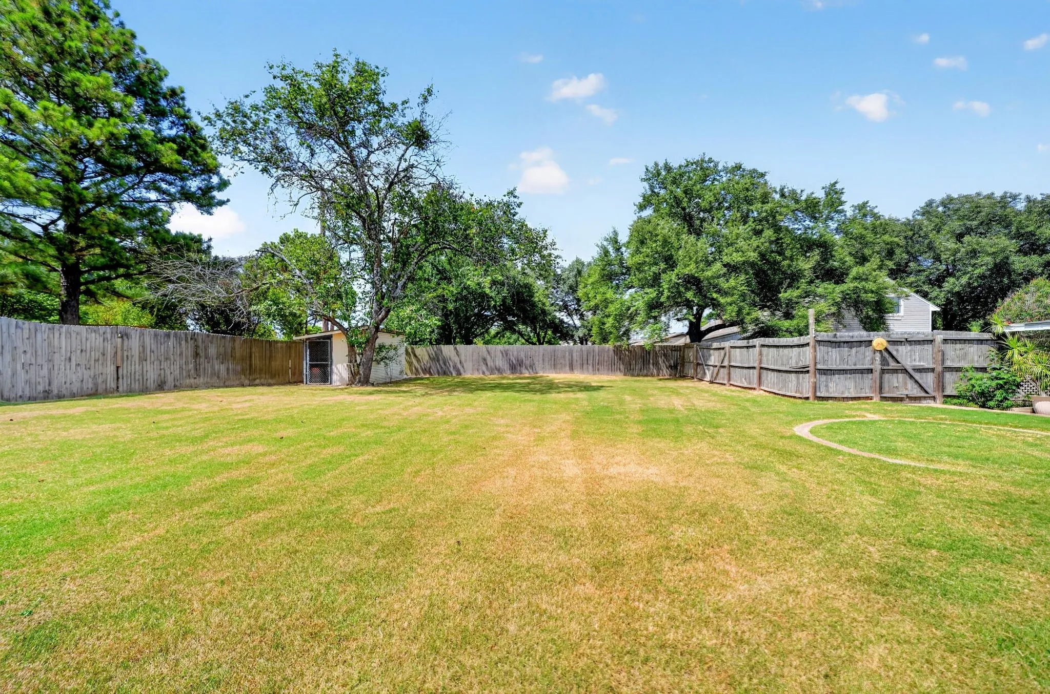 Expansive lawn area, mature trees, wood privacy fencing, and an outdoor storage structure