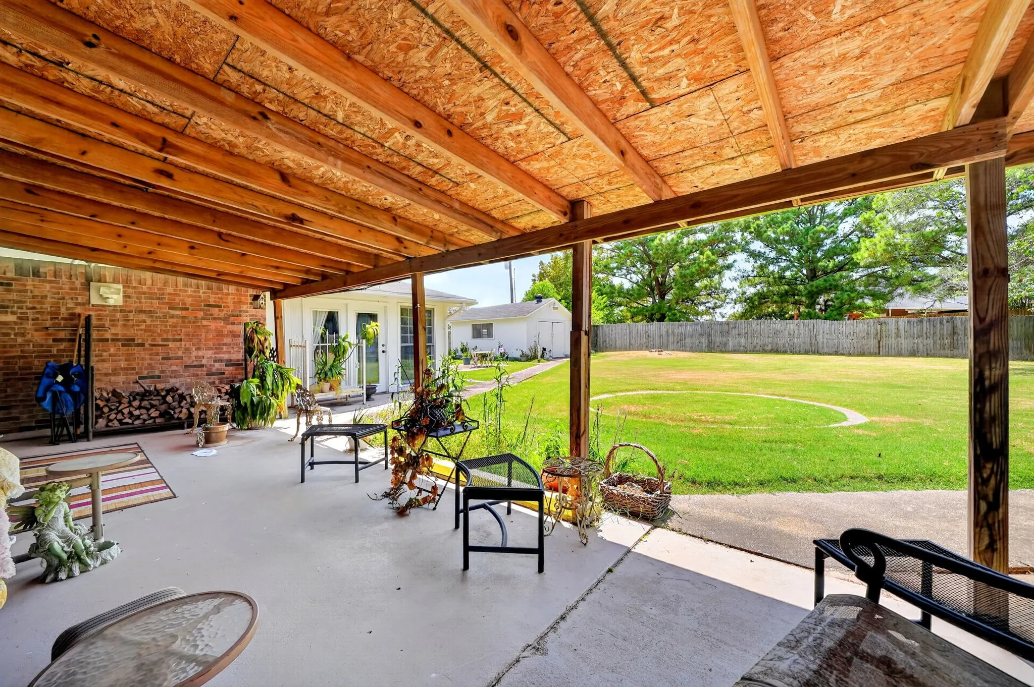 Expansive covered patio with exposed wood ceiling beams, brick exterior wall, and concrete flooring